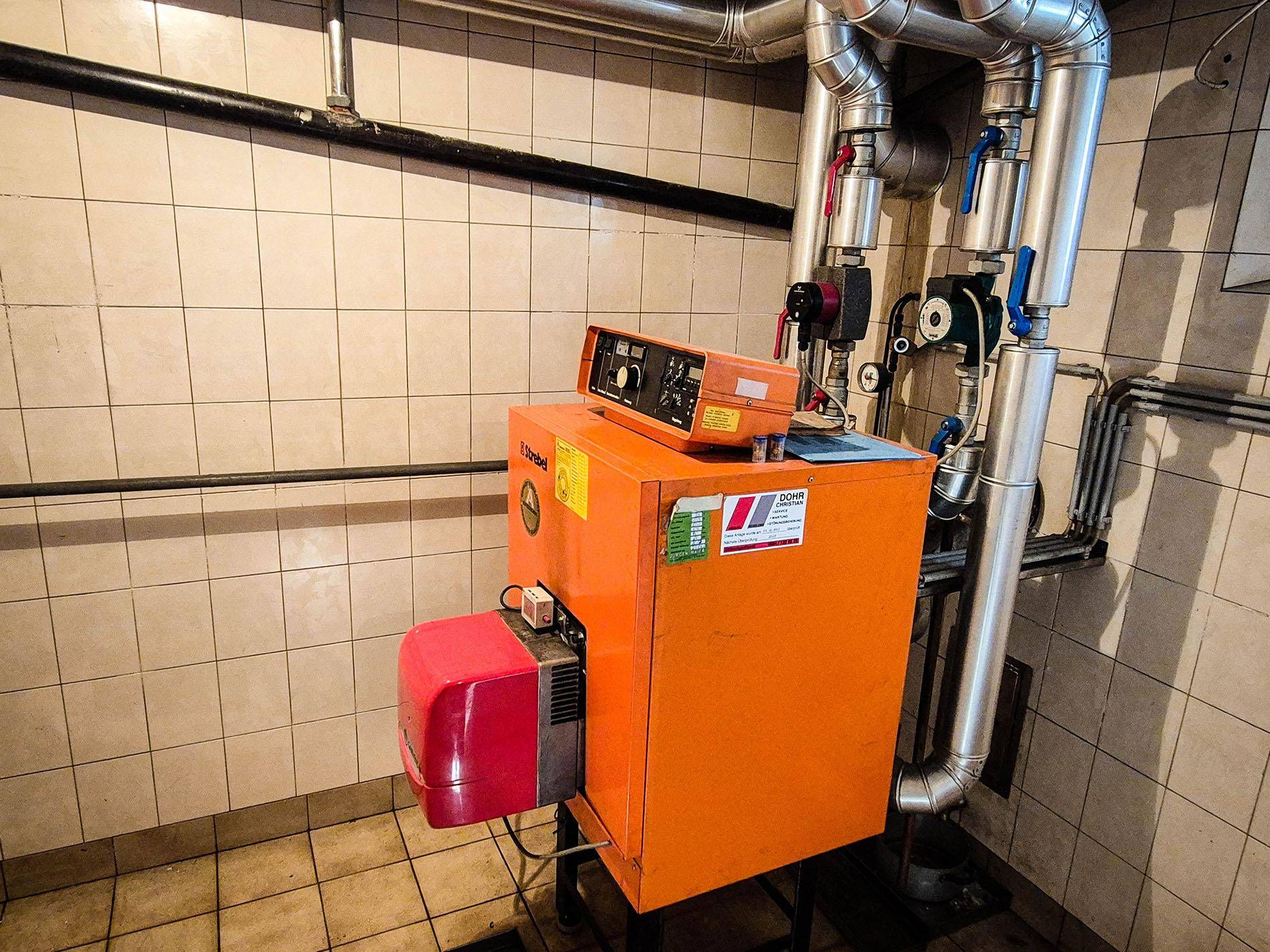 Heizungsraum mit einem orangefarbenen Heizkessel und sichtbaren Rohren.