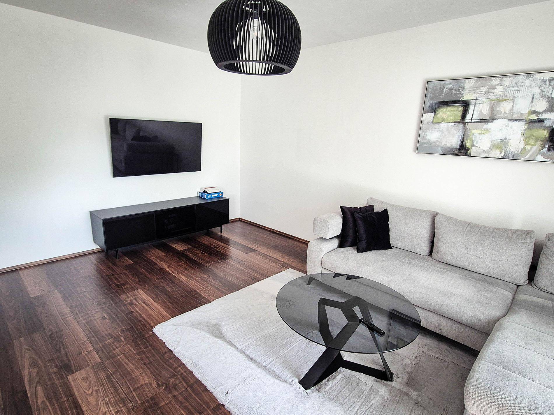 Modernes Wohnzimmer mit dunklem Holzboden, grauem Sofa und einem wandmontierten Fernseher.