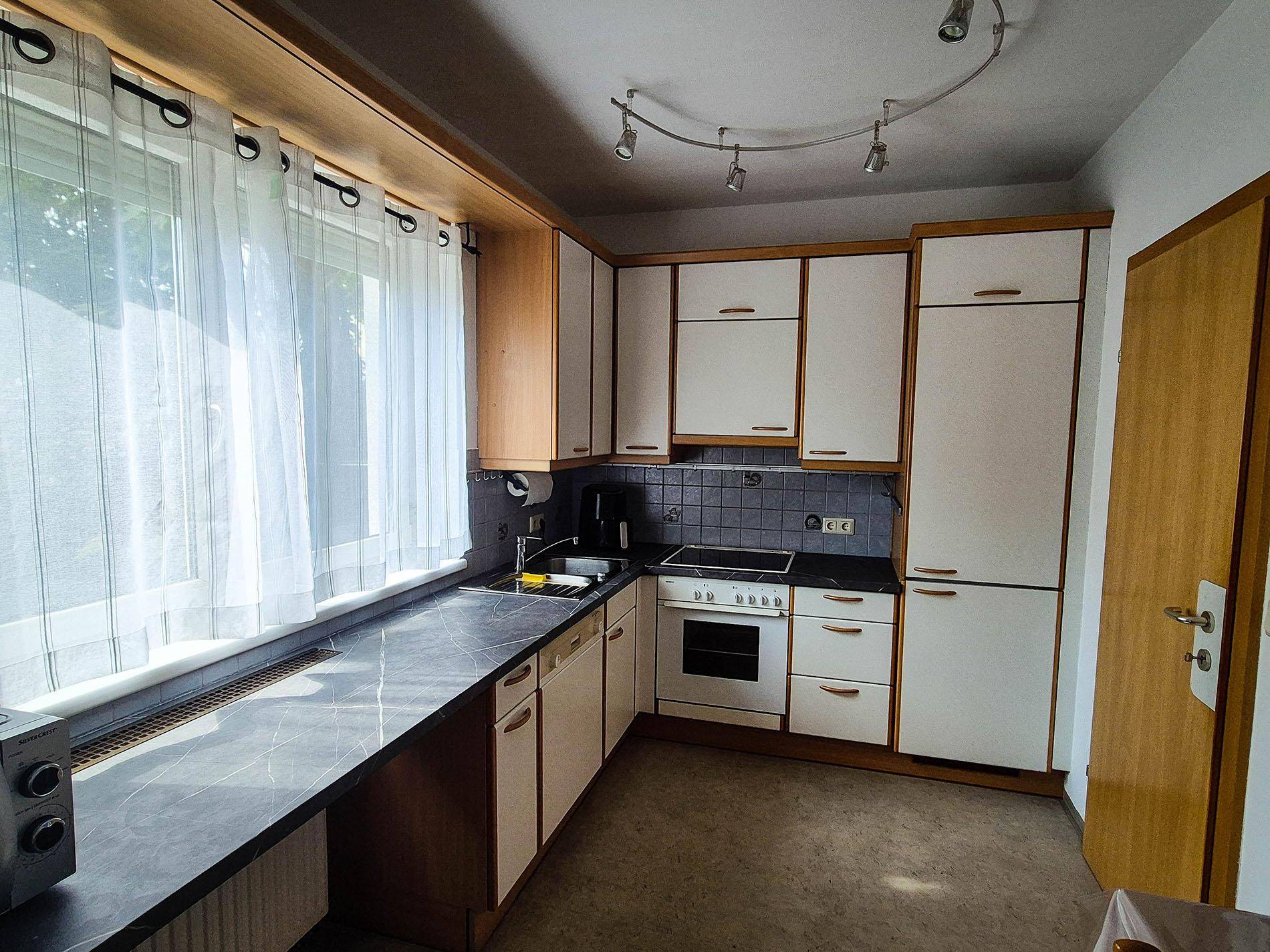 Küche mit hellen Holz- und weißen Schränken, dunkler Arbeitsplatte und einem Fenster.