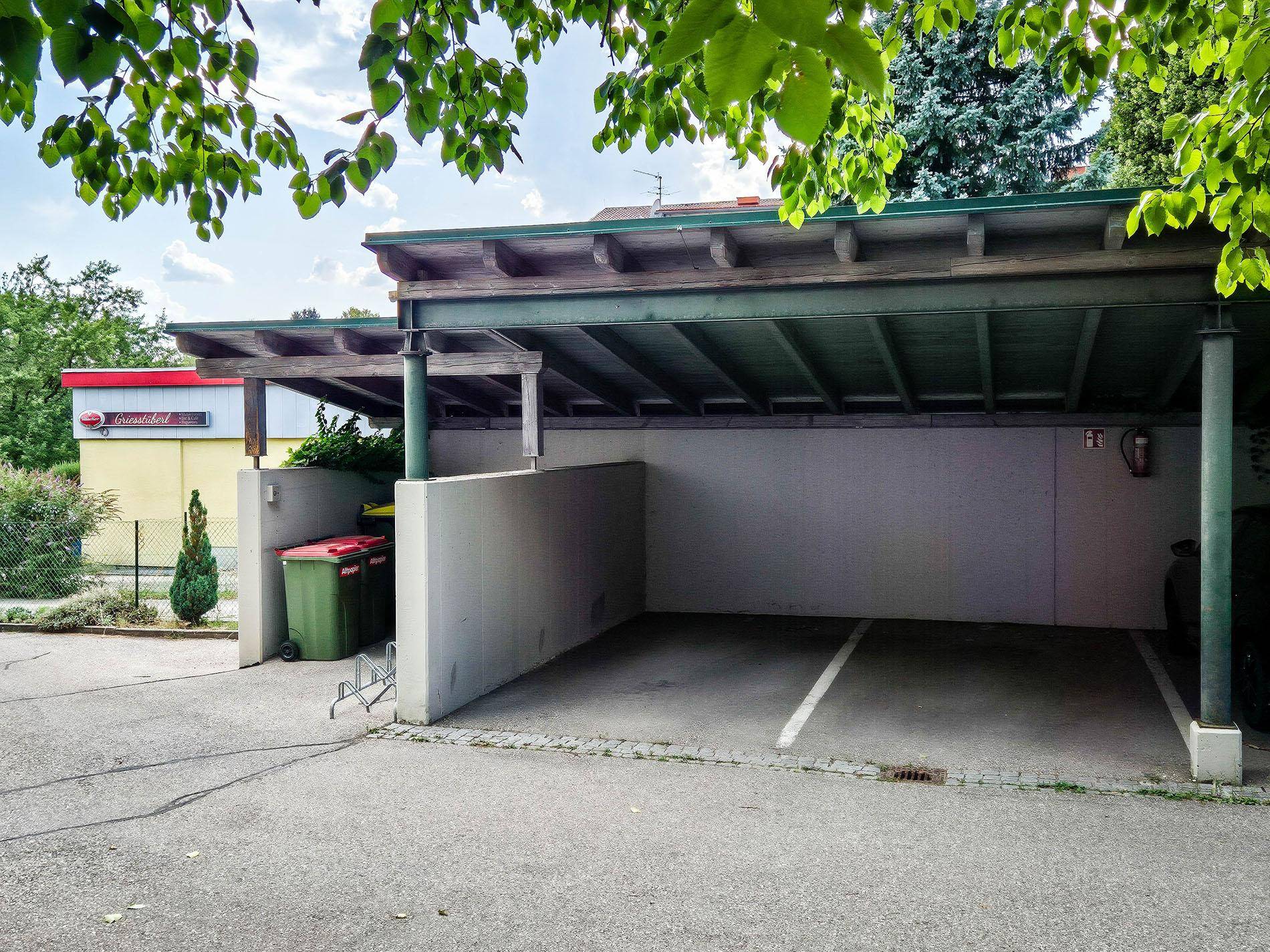 Überdachter Carport mit einem freien Stellplatz und einem Mülleimer im Außenbereich.