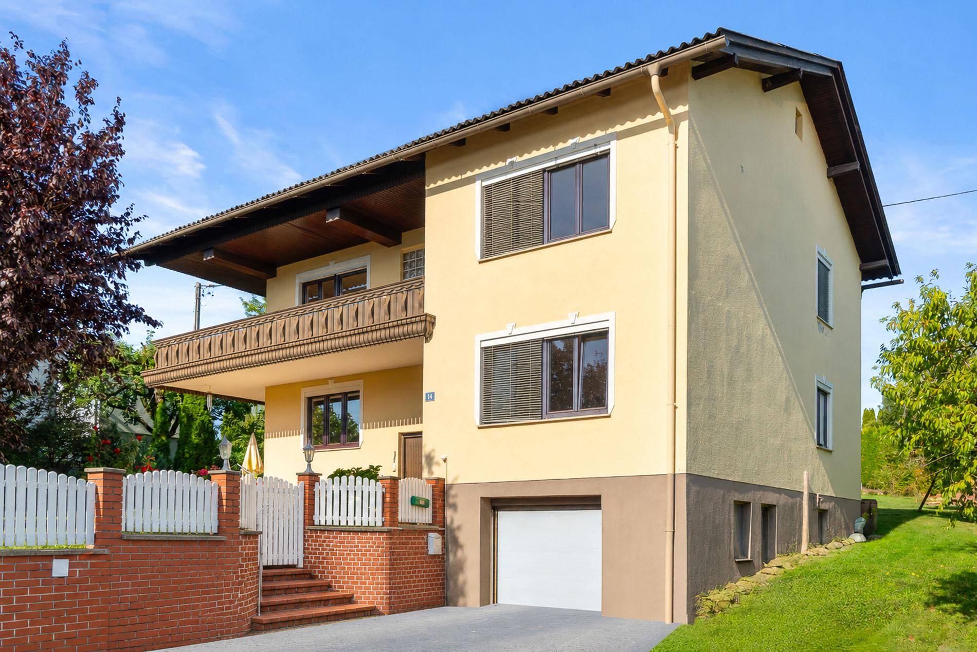 Gelbes Einfamilienhaus mit Satteldach, Balkon und integrierter Garage in gepflegter Umgebung.