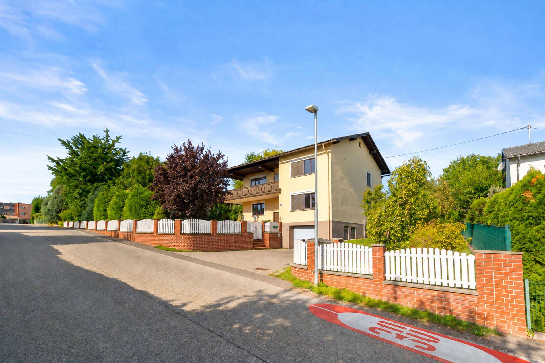 Einfamilienhaus in ruhiger Wohngegend mit viel Grün und gepflegtem Vorgarten von der Straße aus gesehen.