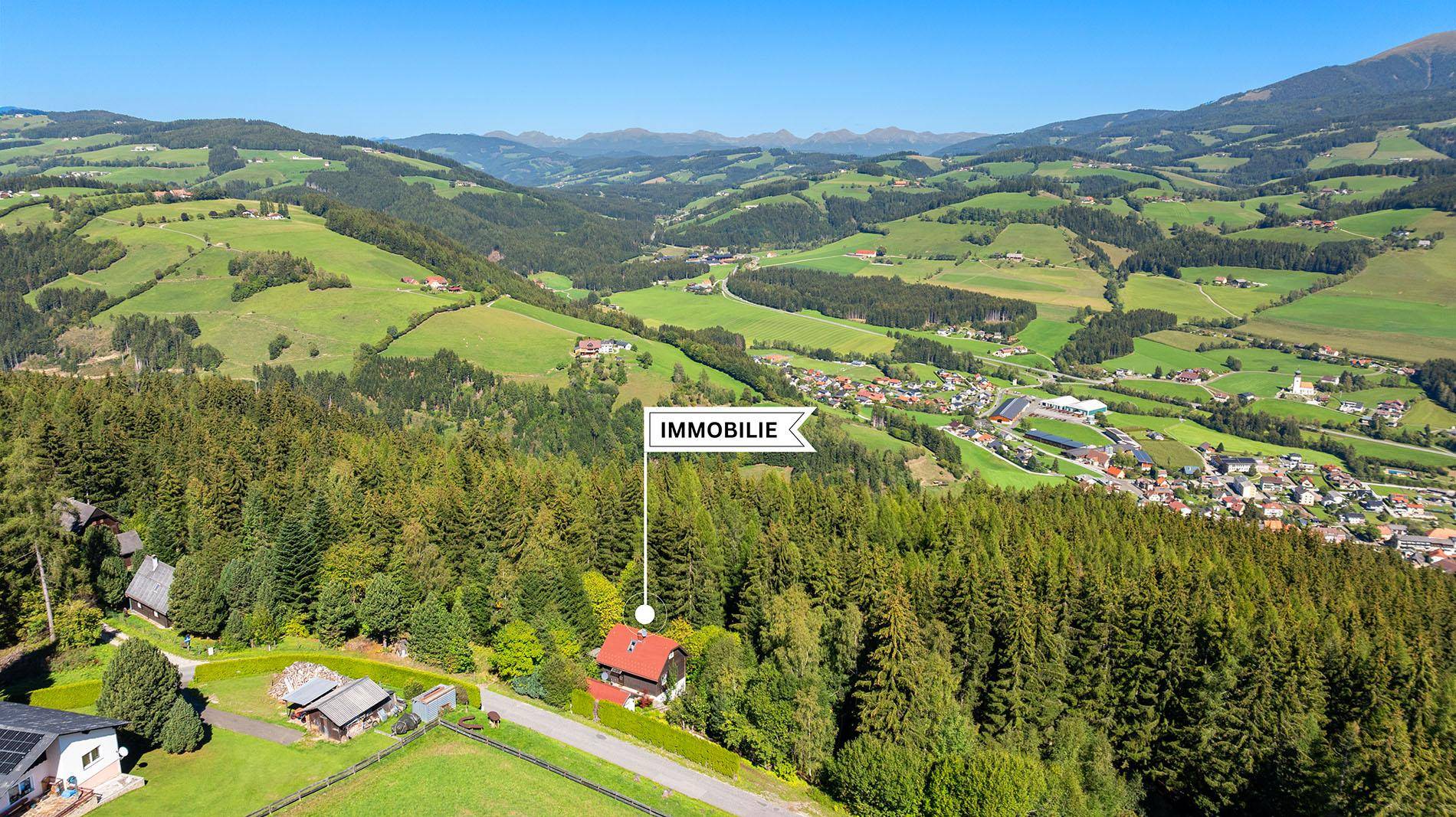 Weitläufige Luftaufnahme der Immobilie in einer grünen Hügellandschaft mit Wald und Dorf.