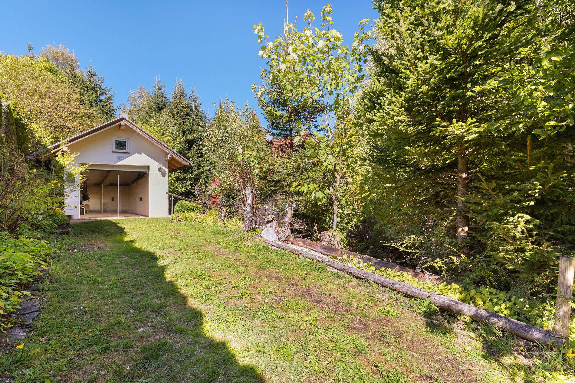 Grüner Weg führt zu einer hellen Garage, umgeben von Bäumen und natürlicher Landschaft.