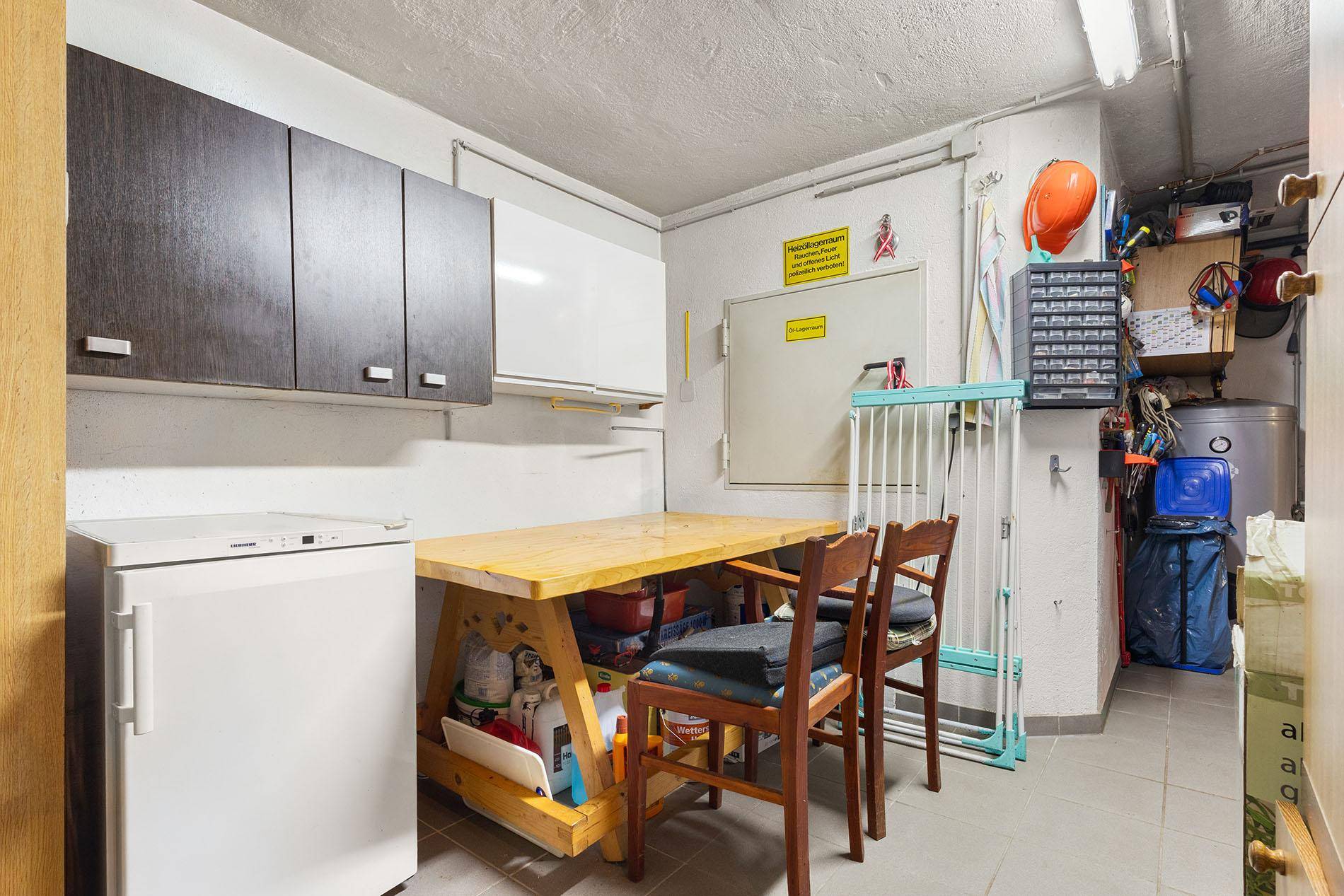 Praktischer Abstellraum mit Tisch, Kühlschrank und Regalen für diverse Gegenstände.