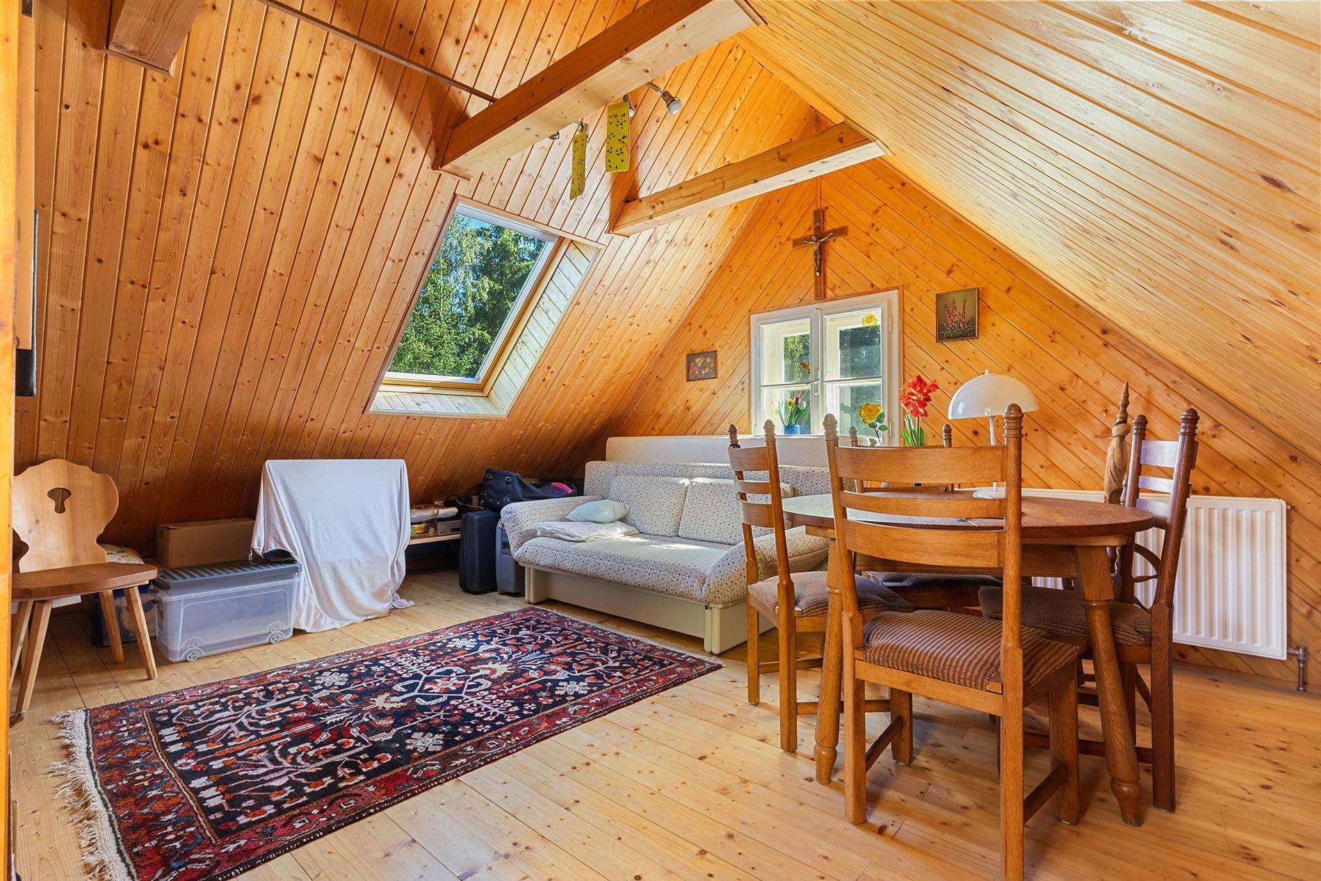 Gemütlicher Dachbodenraum mit Holzvertäfelung, Dachfenster und Schlaf- oder Wohnbereich.