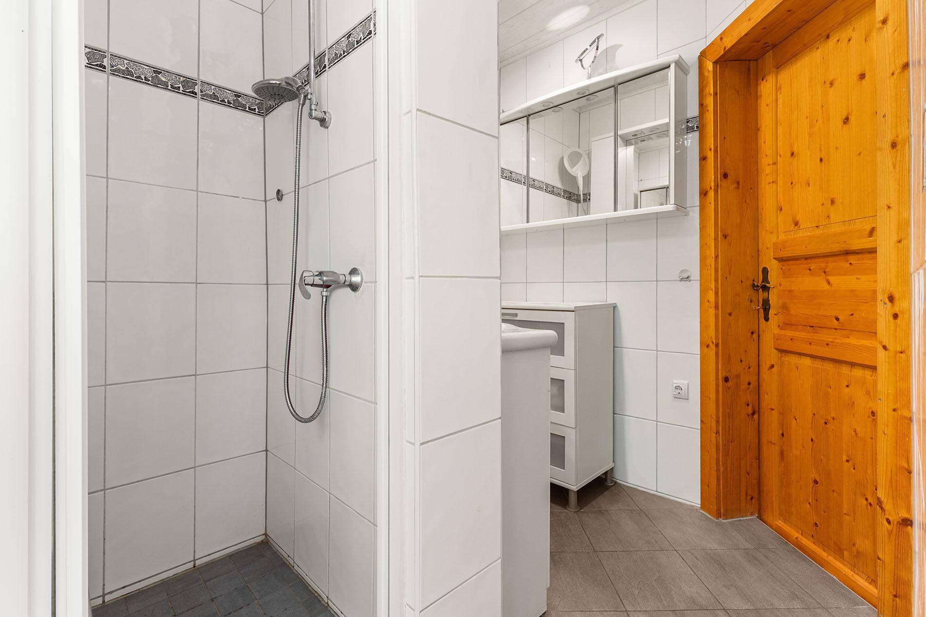 Einfaches Badezimmer mit weißen Fliesen, Duschbereich und Holzinnentür.