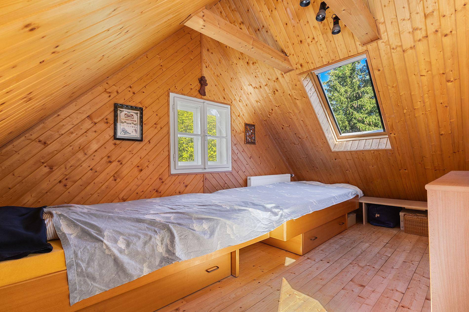 Helles Dachzimmer mit Holzvertäfelung, Holzboden und einem Bett unter dem Dachfenster.