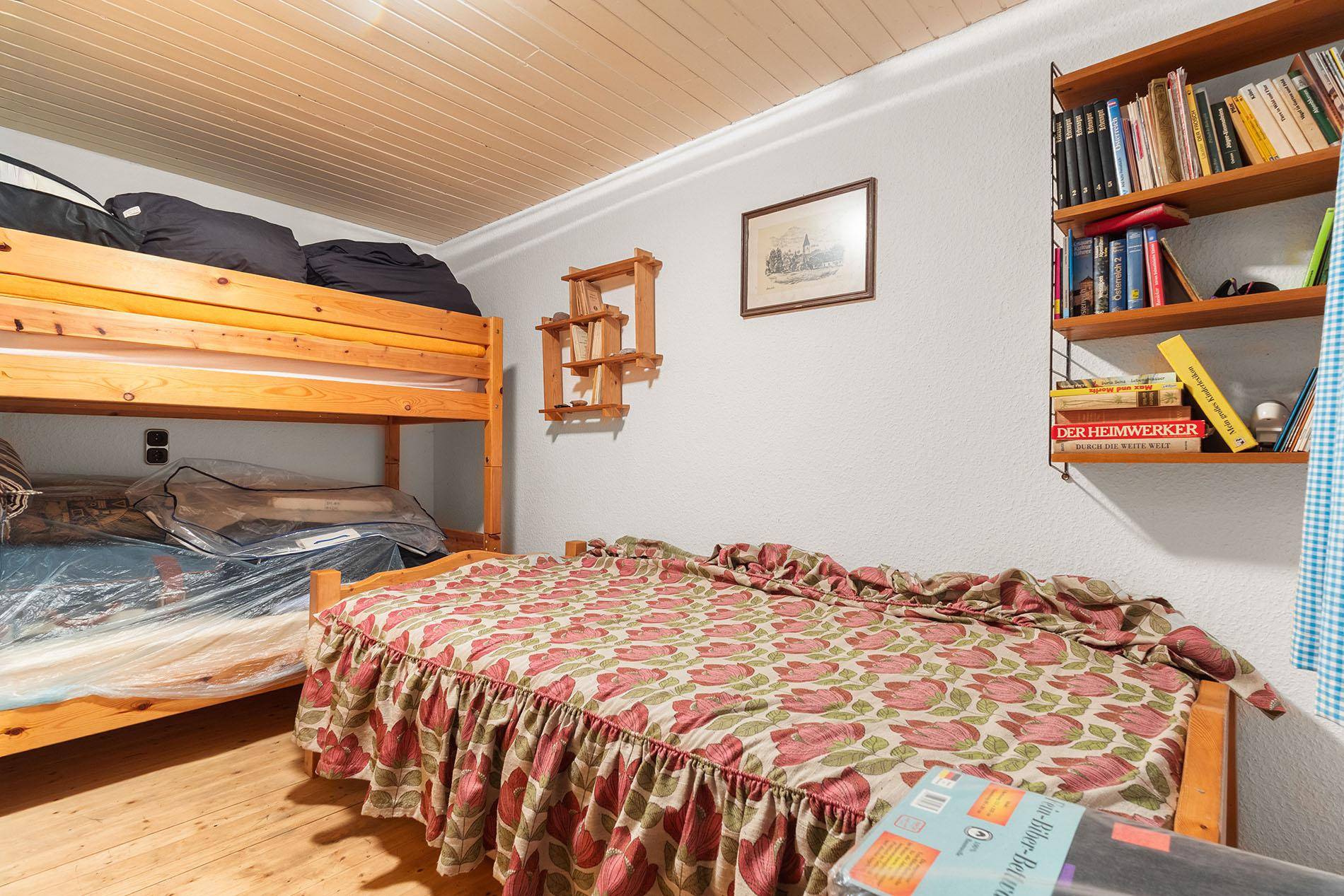 Schlafzimmer mit Etagenbett und Einzelbett, Holzboden und einfacher Einrichtung.