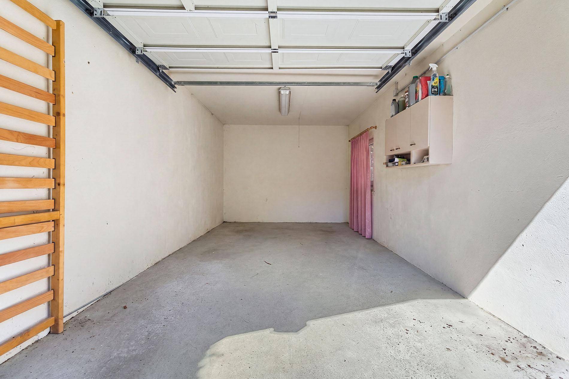 Leere Garage mit Betonboden, weiß gestrichenen Wänden und Garagentor.