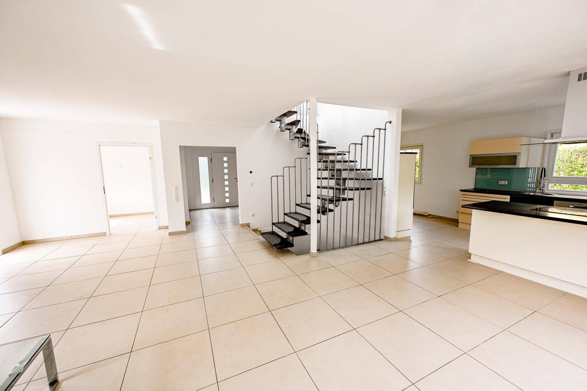 Großzügiger Wohnbereich mit offener Küche, Fliesenboden und moderner Treppe.