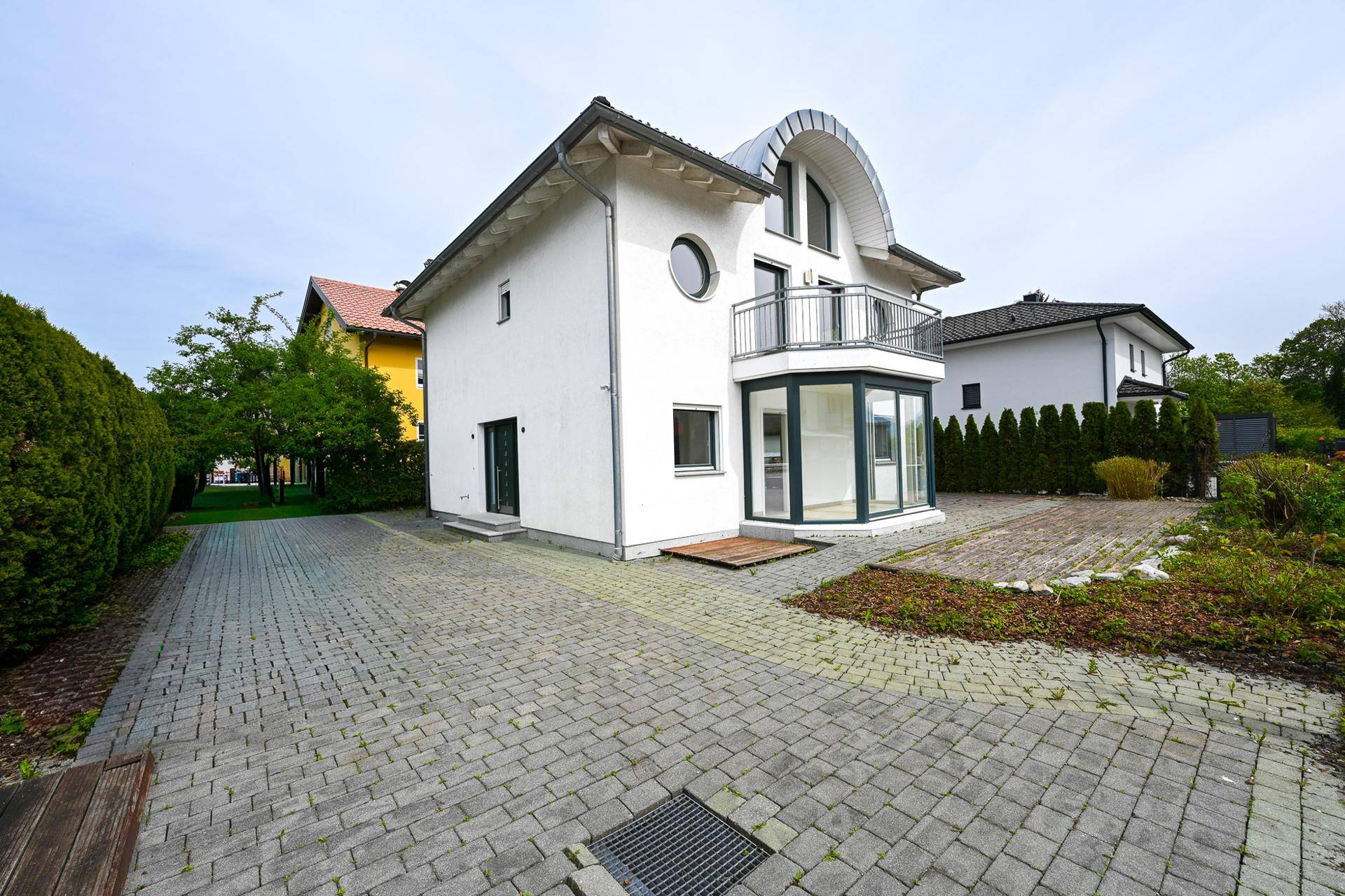 Seitenansicht des Hauses mit gepflasterter Auffahrt und grüner Hecke.