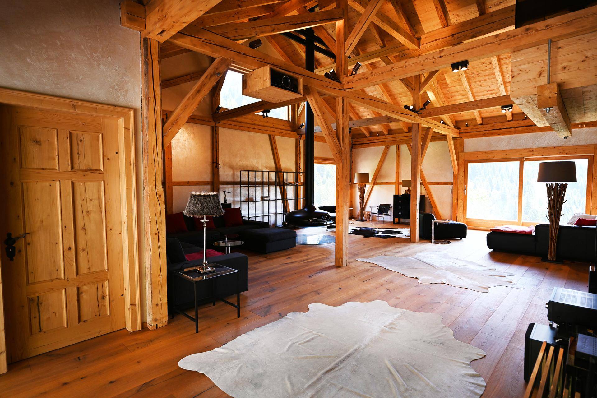 Weitläufiges Wohnzimmer mit offener Holzkonstruktion, großen Fenstern und modernem Kamin, sehr hell.