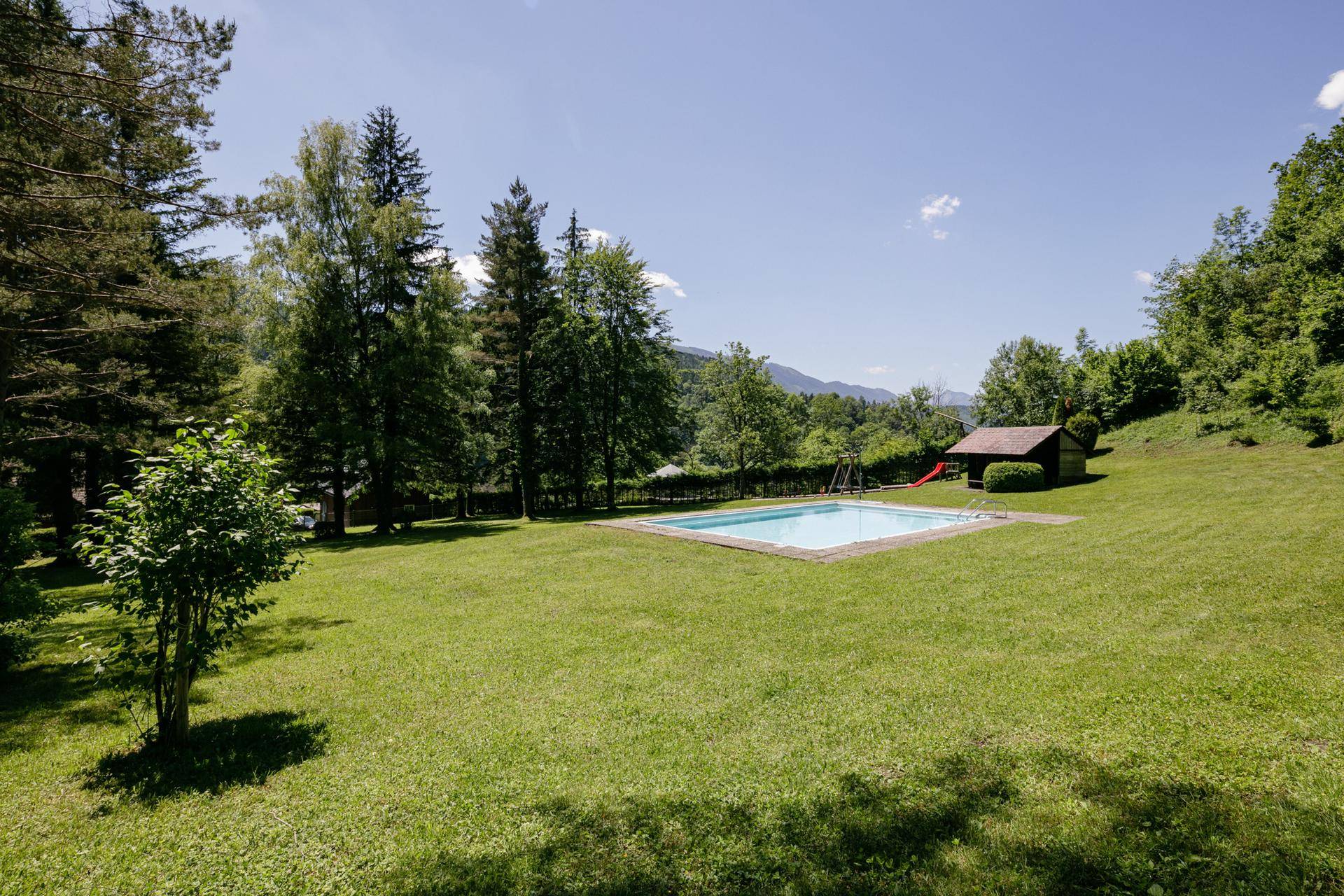 Großer Garten mit Swimmingpool und Kinderspielplatz, umgeben von Bäumen und einer weiten Landschaft.