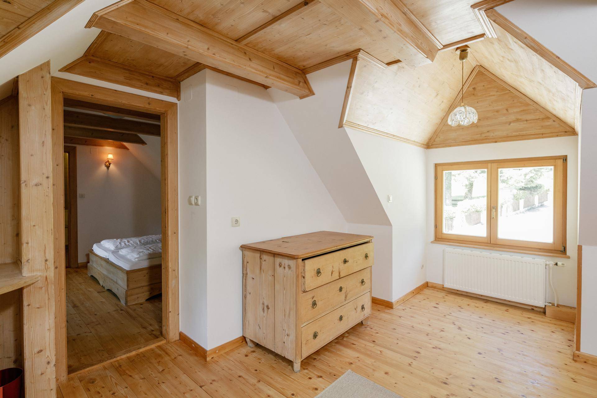 Helles Schlafzimmer im Dachgeschoss mit Holzboden, schrägen Decken und einem Fenster mit Blick ins Grüne.