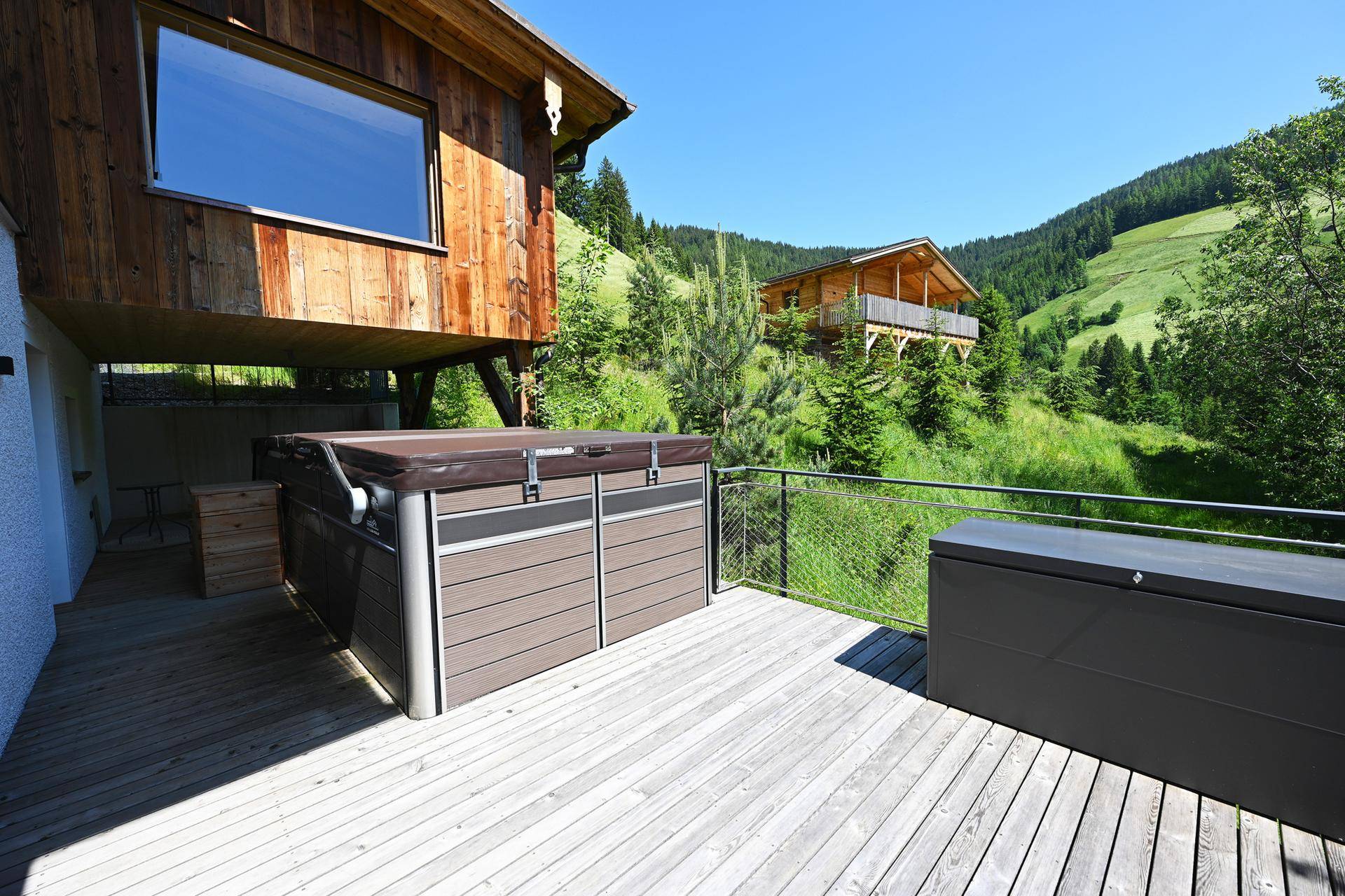 Geräumige Holzterrasse mit Whirlpool und Panoramablick auf die umliegende grüne Berglandschaft.