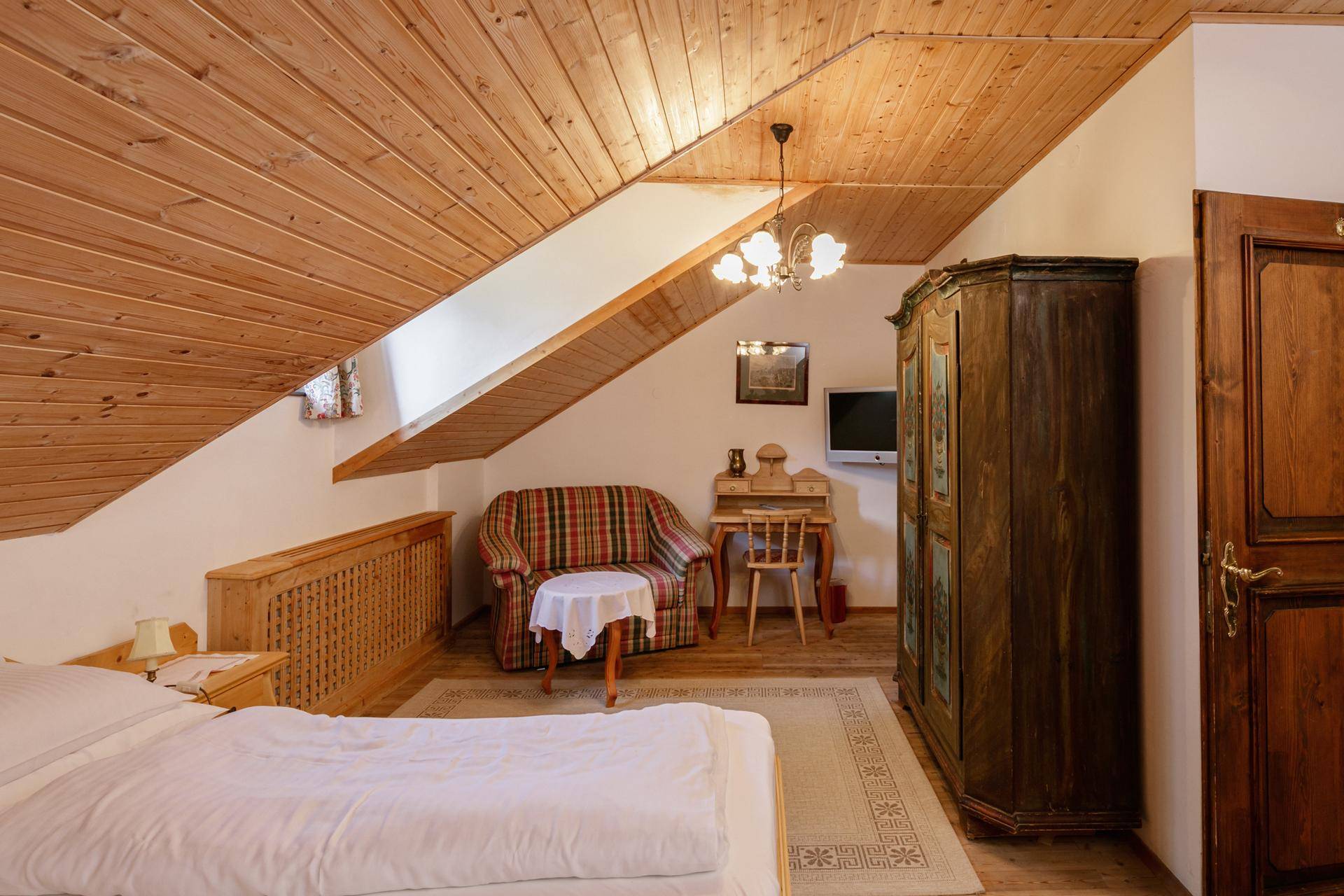 Gemütliches Schlafzimmer im Dachgeschoss mit Holzdecke, schrägen Wänden und traditionellen Möbeln.