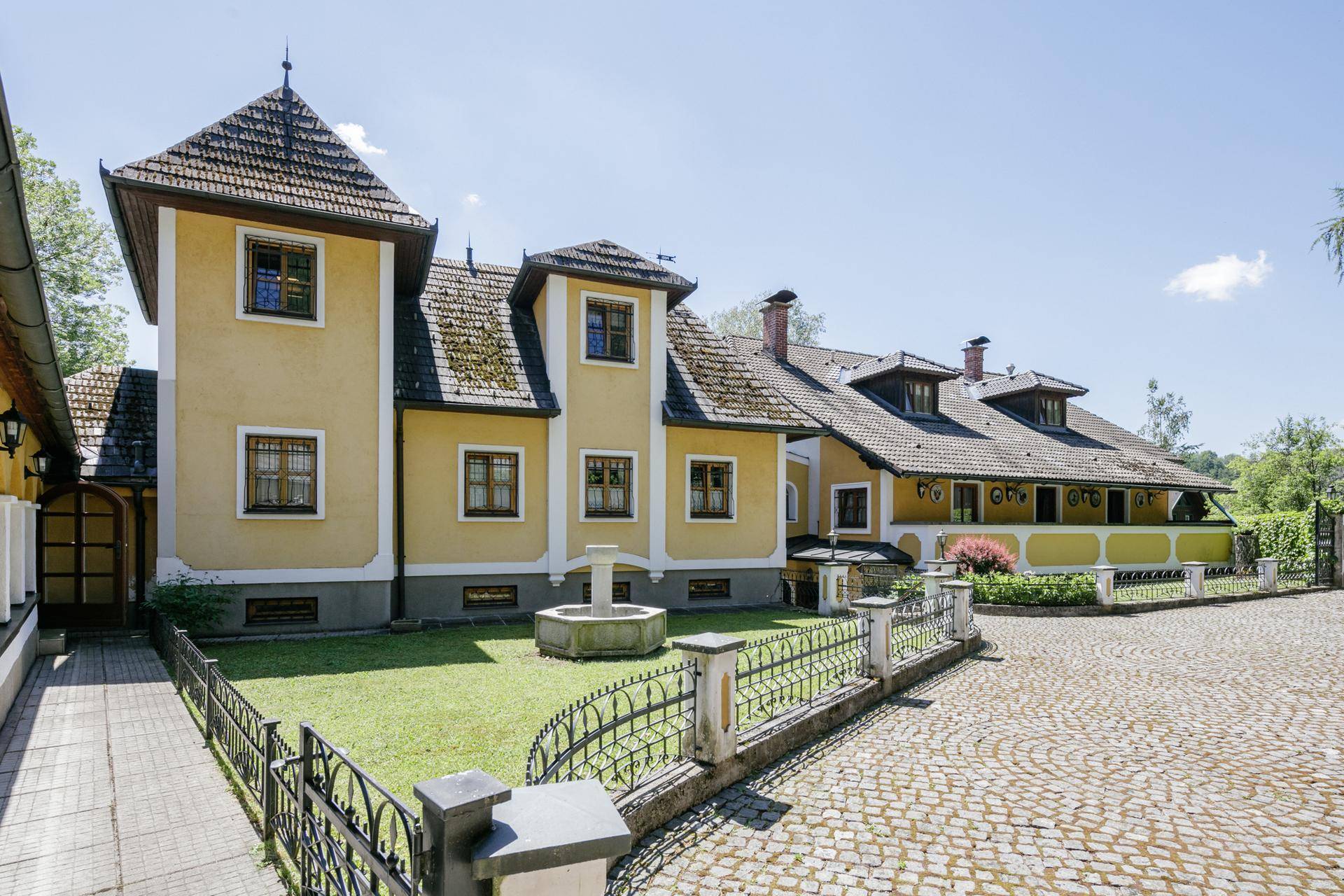 Historisches Gebäude mit gelber Fassade, Türmchen und gepflegtem Vorgarten mit Brunnen.