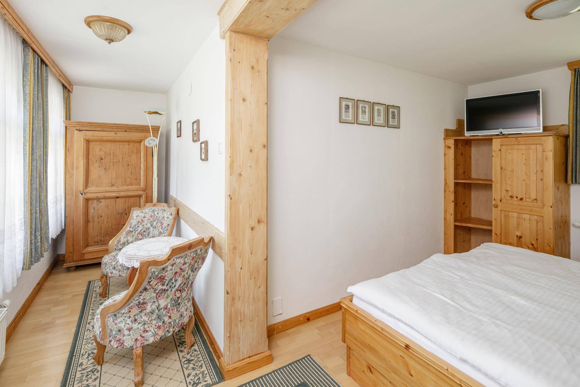 Helles Schlafzimmer mit Holzboden, traditionellen Möbeln und einem sichtbaren Holzbalken.