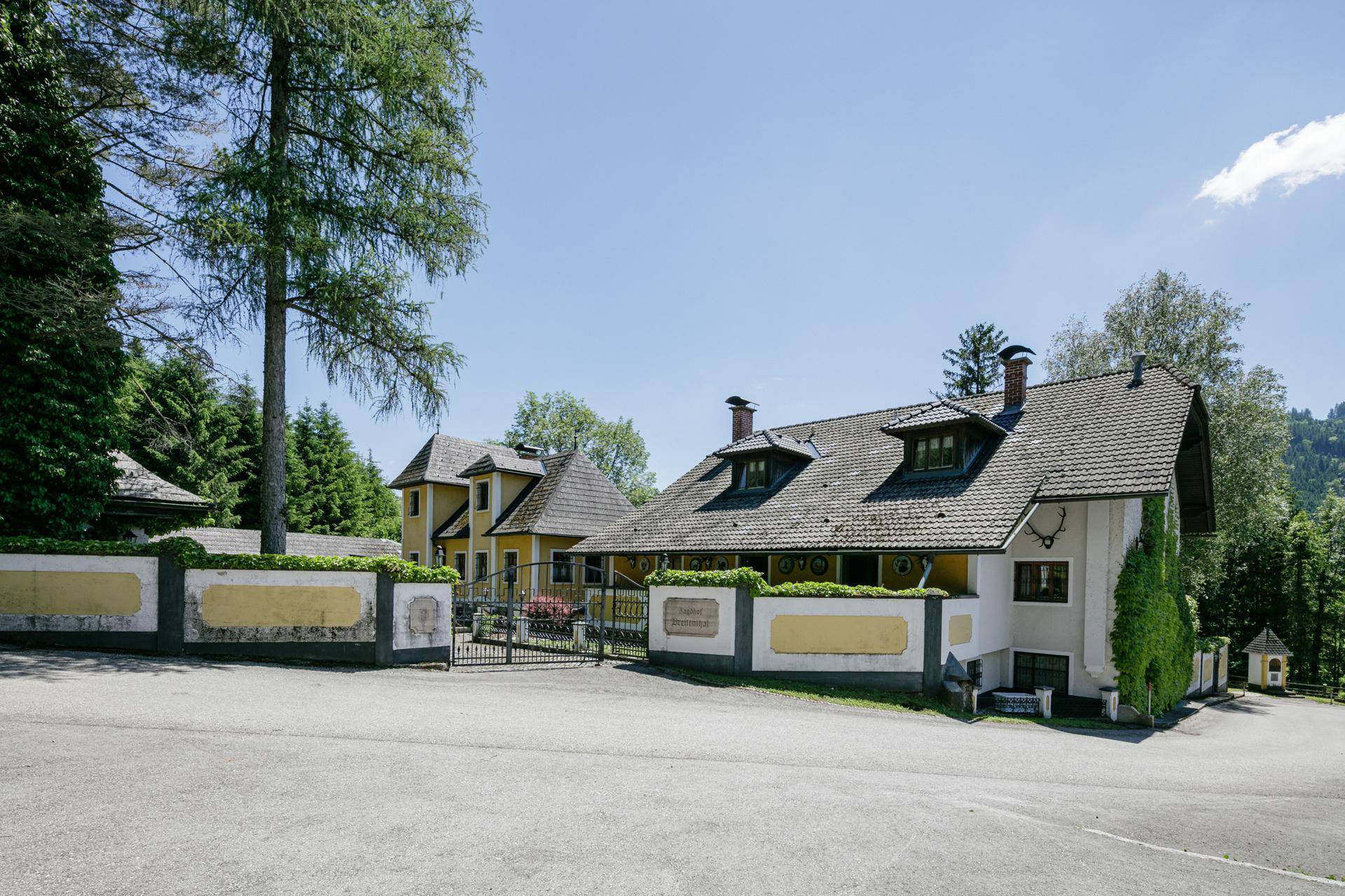 Historisches Anwesen mit schmiedeeisernem Tor, umgeben von Bäumen und einer gepflegten Hecke.