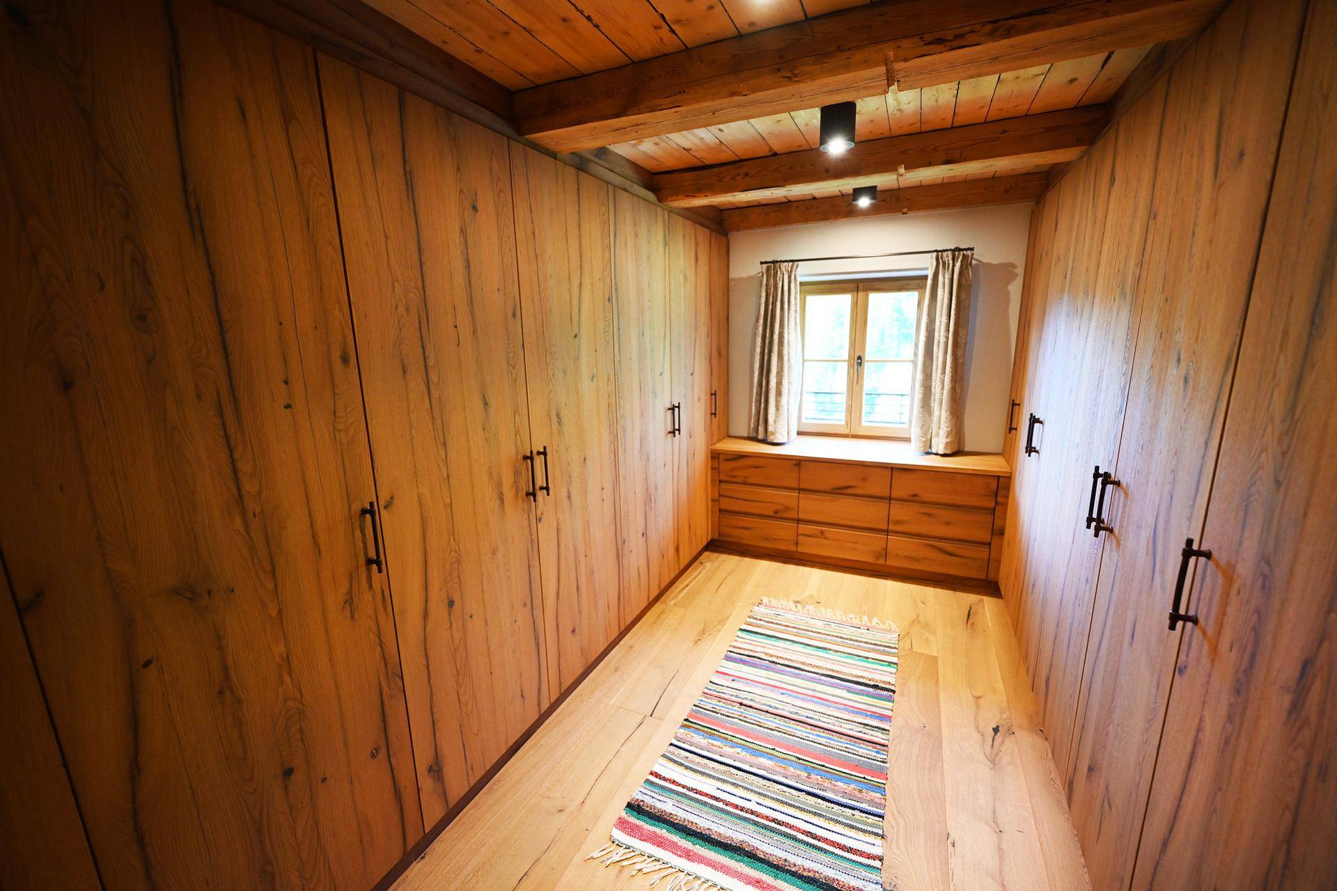 Begehbarer Kleiderschrank mit maßgefertigten Holzschränken und Holzbalkendecke.