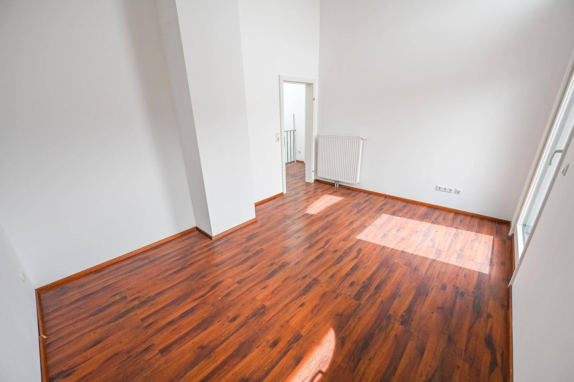 Lichtdurchflutetes Zimmer mit Laminatboden und Zugang zum Flur.