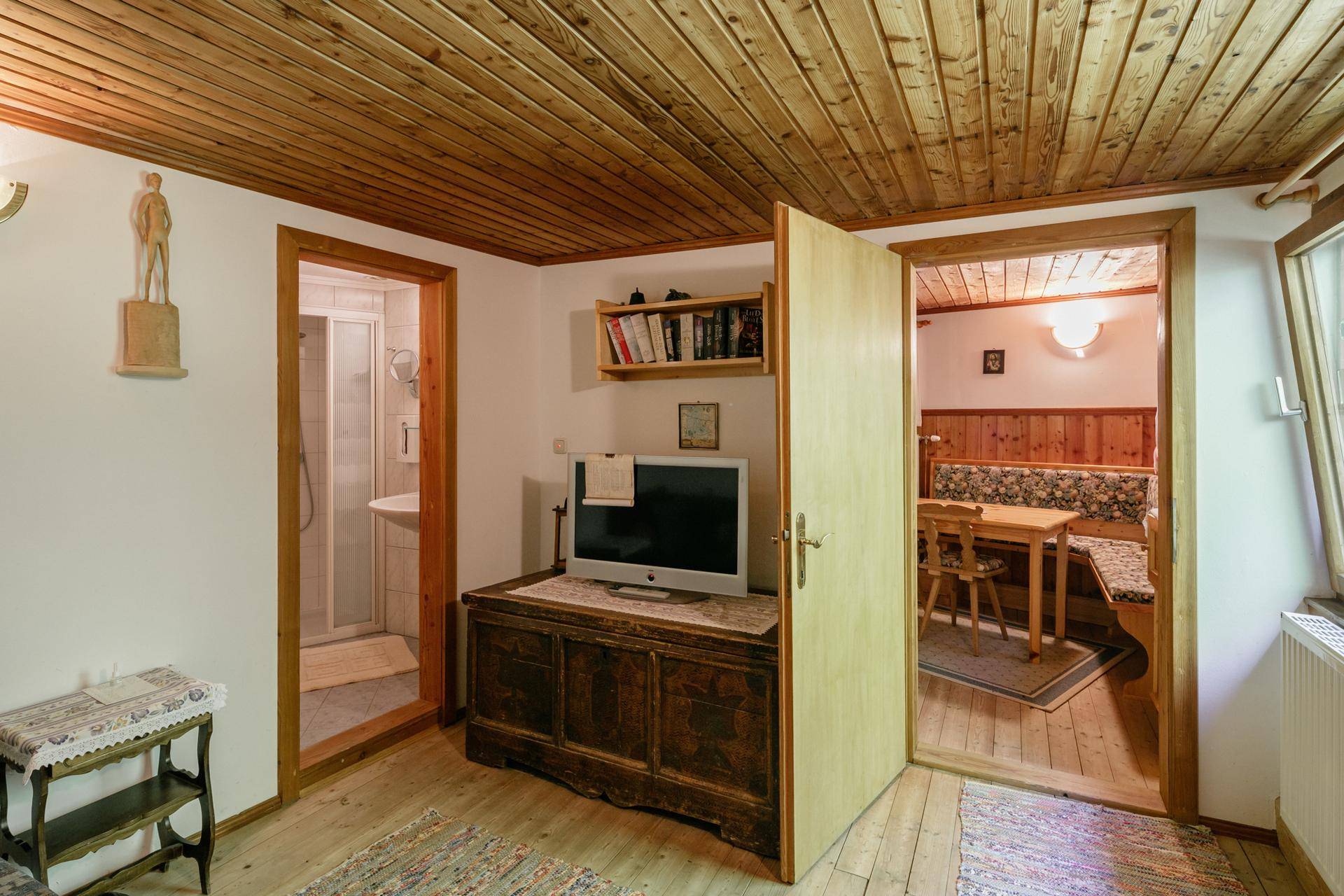 Wohnbereich mit Holzboden, Fernseher und Zugang zu Küche und Badezimmer.