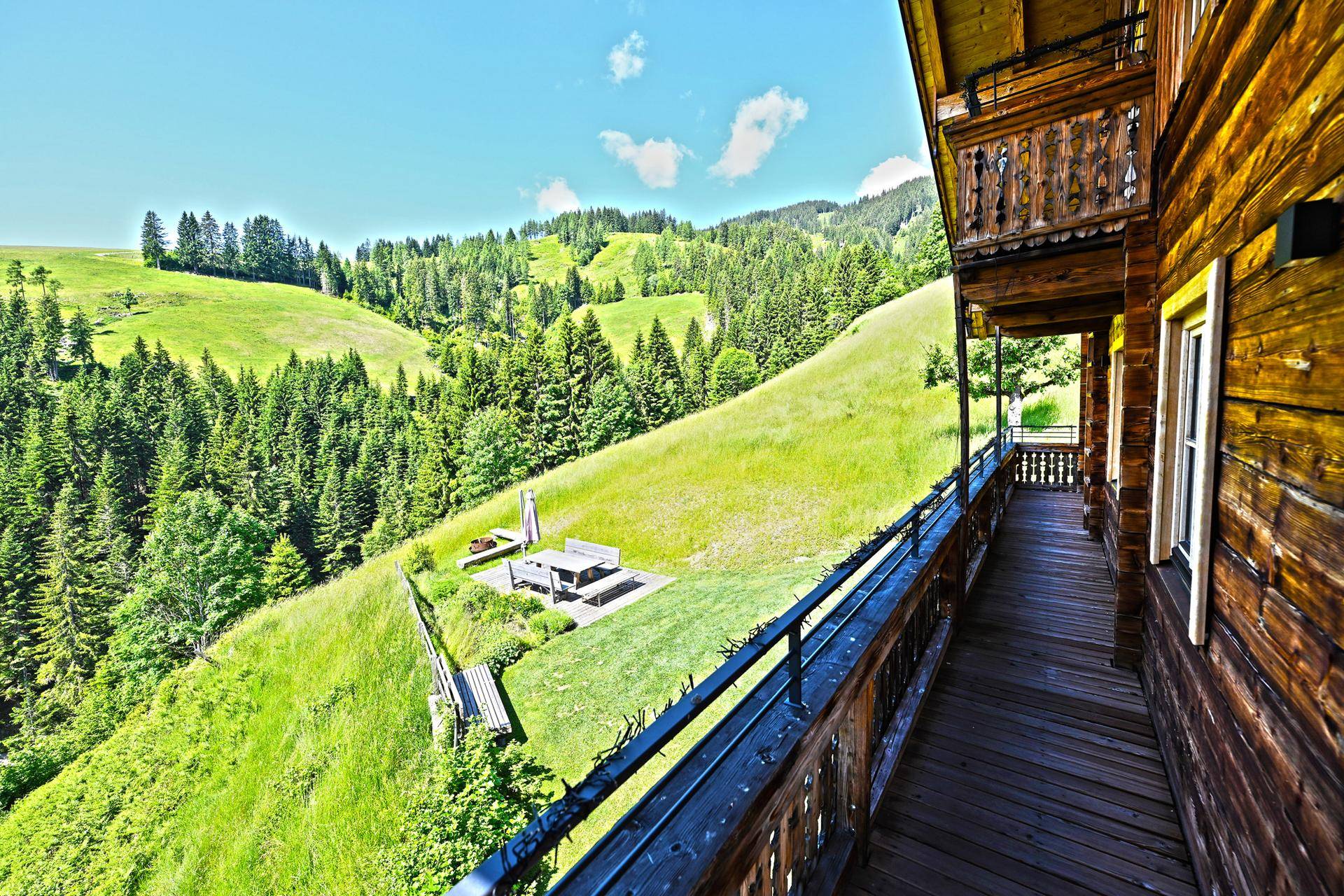 Langer Holzbalkon mit Geländer und weitem Blick auf die grüne Berglandschaft.
