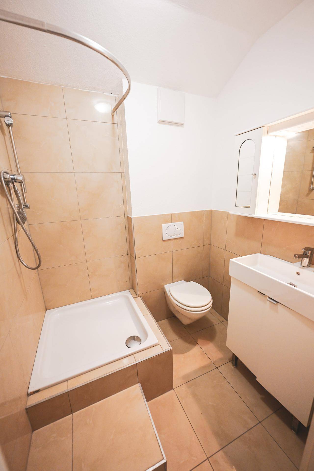 Kleines Badezimmer mit Dusche, WC und Waschbecken.