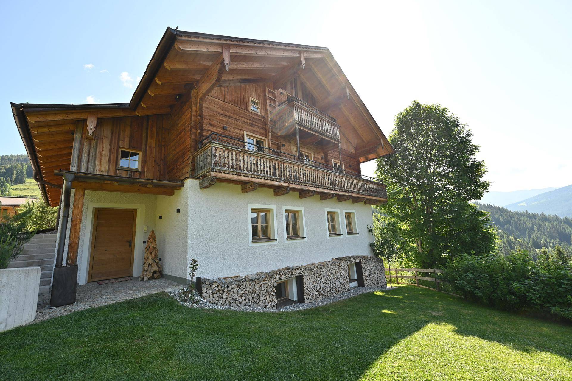 Traditionelles Chalet mit Holzfassade und weiß verputztem Sockel, eingebettet in die alpine Landschaft.