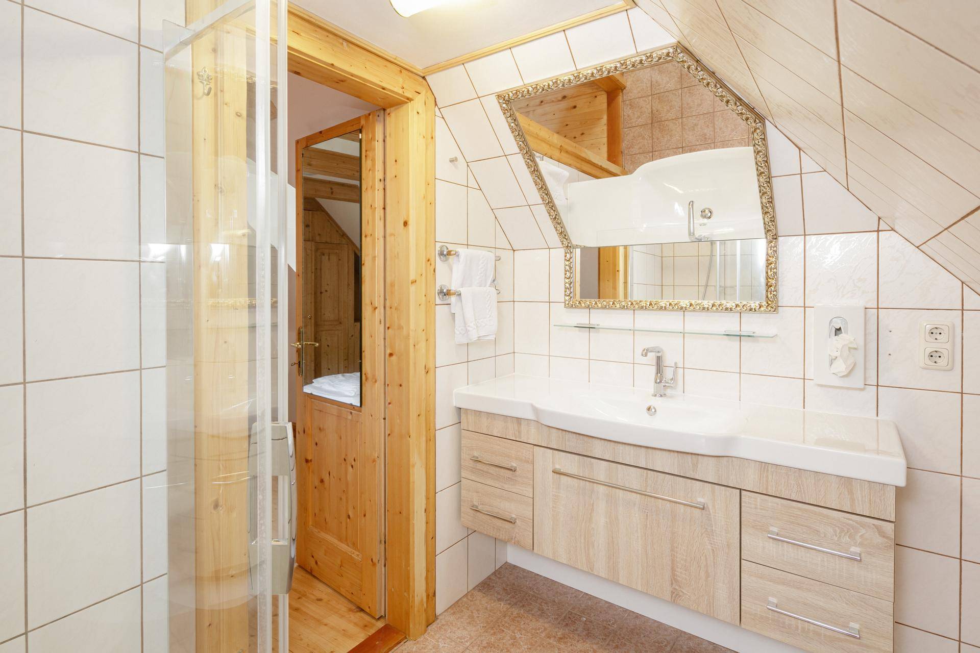 Modernisiertes Badezimmer im Dachgeschoss mit Dusche, Waschtisch und Spiegel unter schräger Decke.