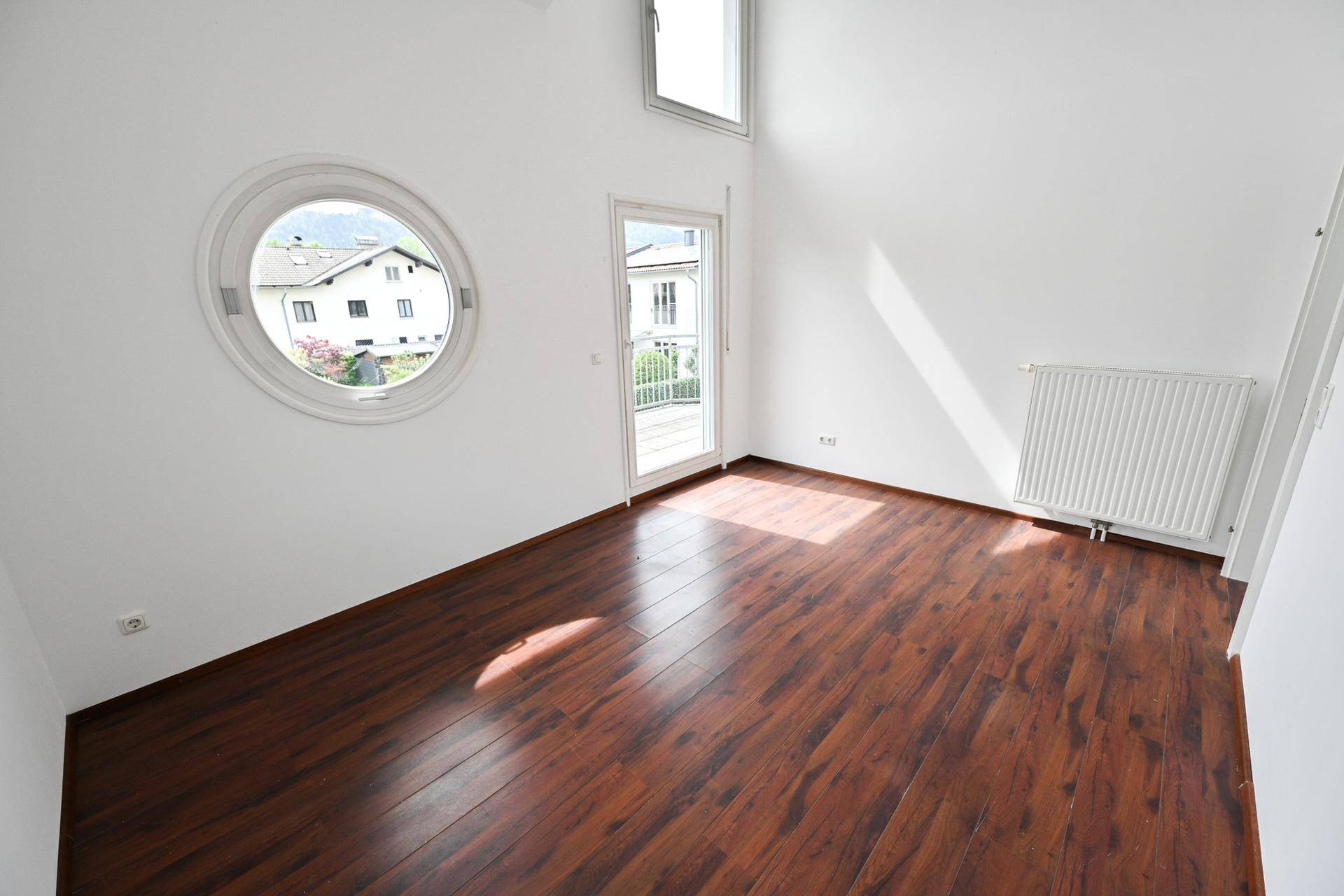 Lichtdurchflutetes Zimmer mit Laminatboden, Rundfenster und Balkonzugang.