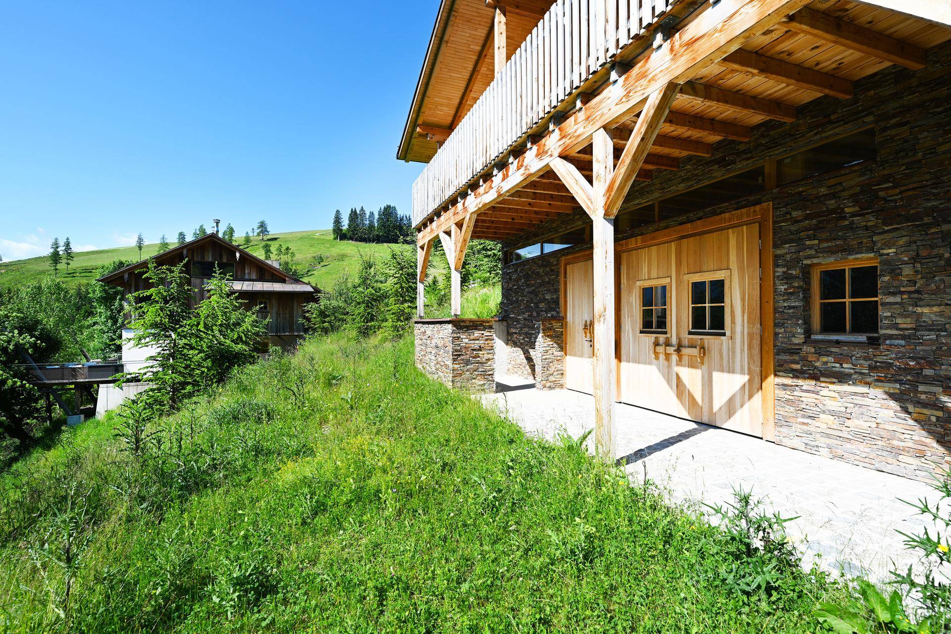 Rustikale Steinfassade mit Holztüren und einem darüberliegenden Holzbalkon, typisch für alpine Architektur.