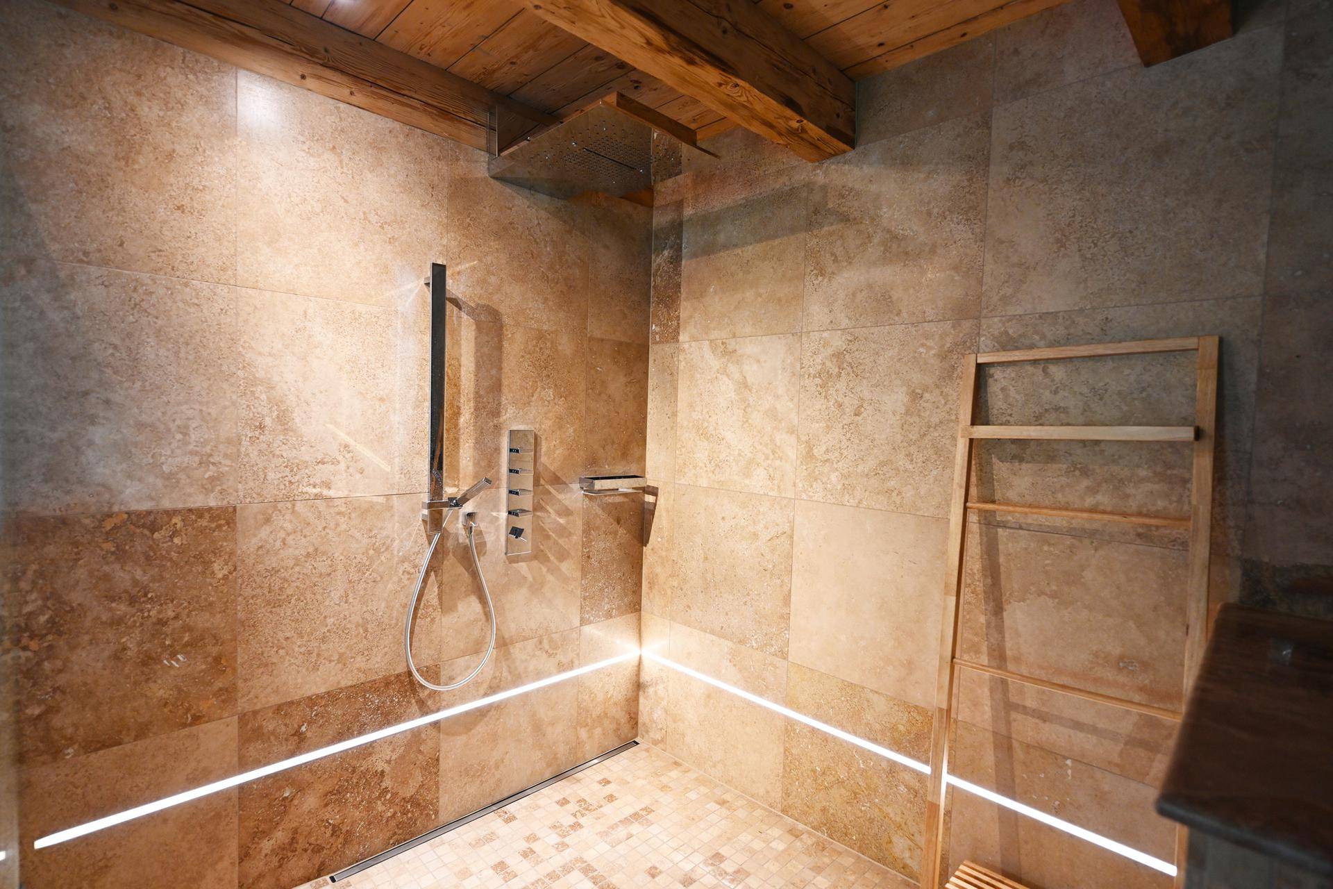 Moderne Dusche mit Natursteinfliesen, Holzbalkendecke und integrierter LED-Beleuchtung für ein entspannendes Ambiente.