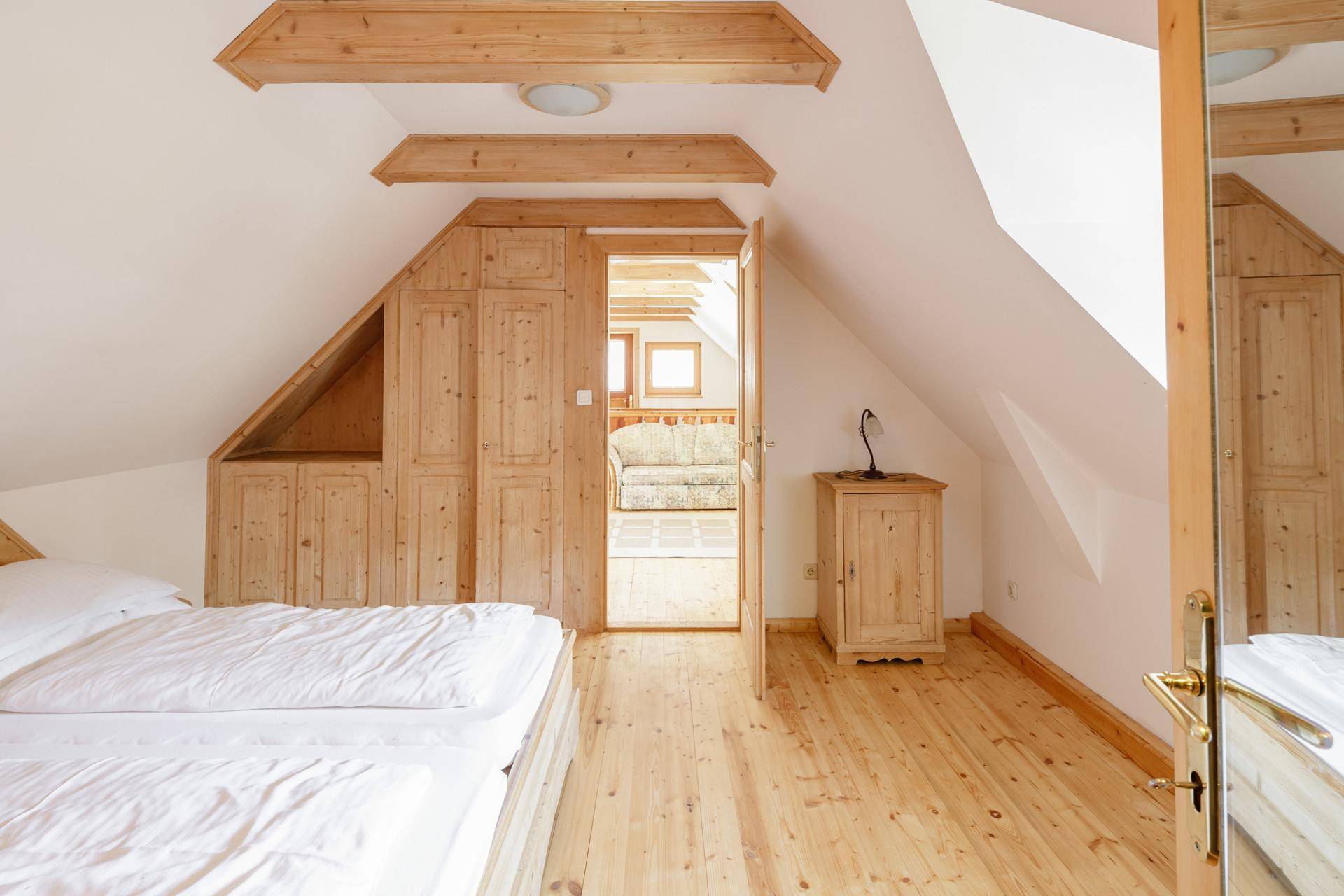 Gemütliches Schlafzimmer im Dachgeschoss mit Holzboden, Einbauschränken und Zugang zu einem weiteren Raum.