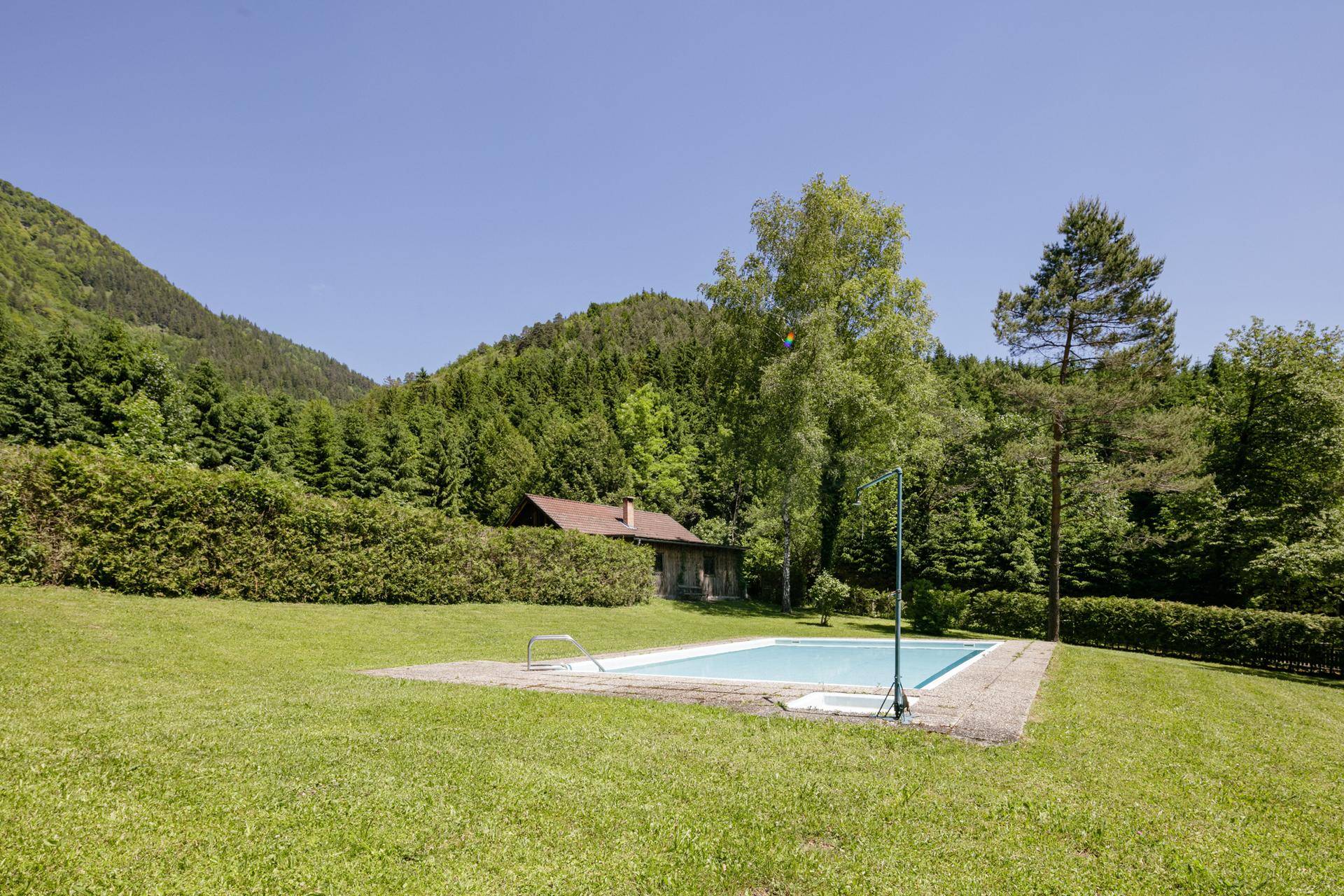 Außenbereich mit Swimmingpool, umgeben von einer großen Rasenfläche und grünen Hügeln.