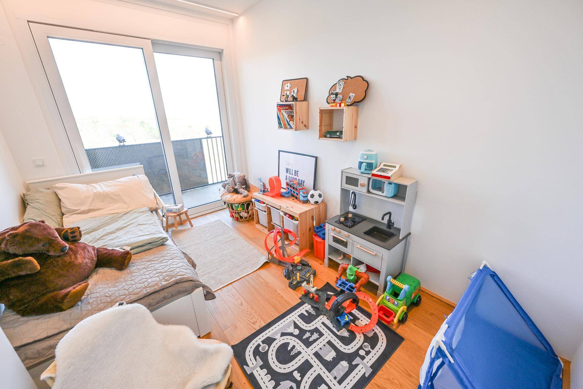 Kinderzimmer mit Spielzeug, Holzboden und Zugang zu einem Balkon.