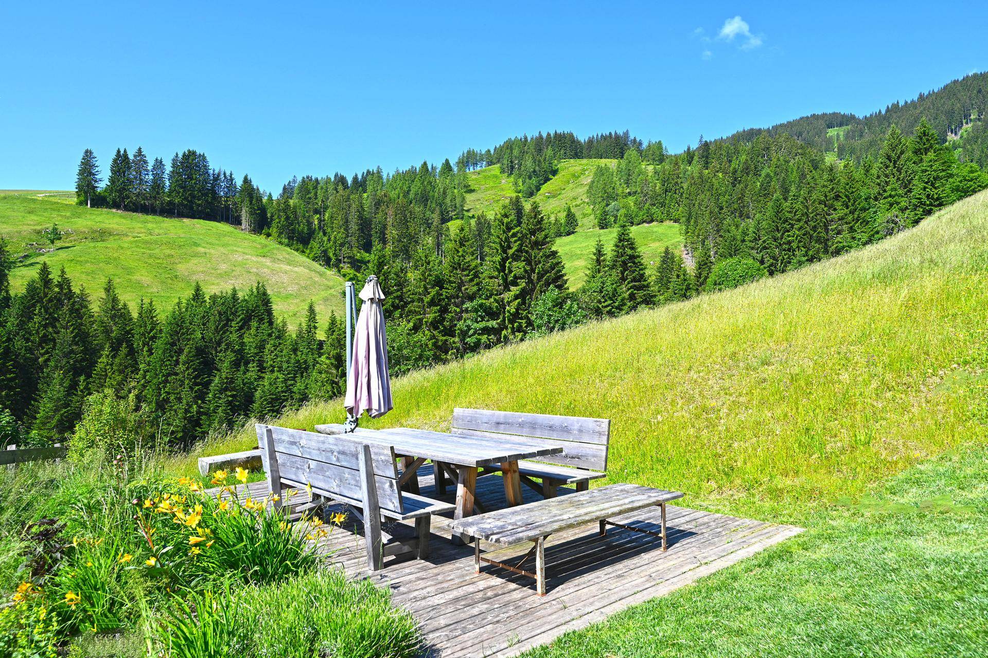 Gemütlicher Sitzbereich im Garten auf einer Holzplattform, ideal für Mahlzeiten im Freien mit Bergblick.