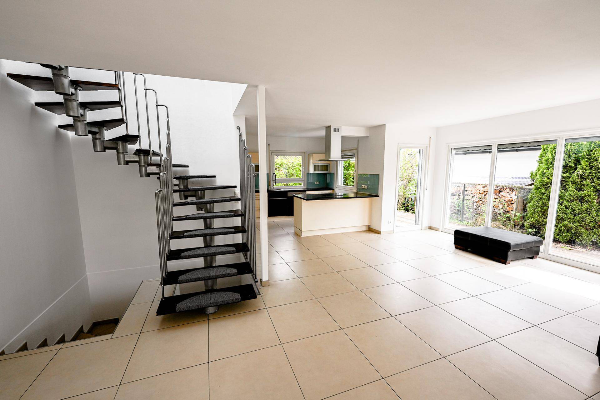 Offener Wohnbereich mit moderner Treppe, Fliesenboden und Blick ins Grüne.