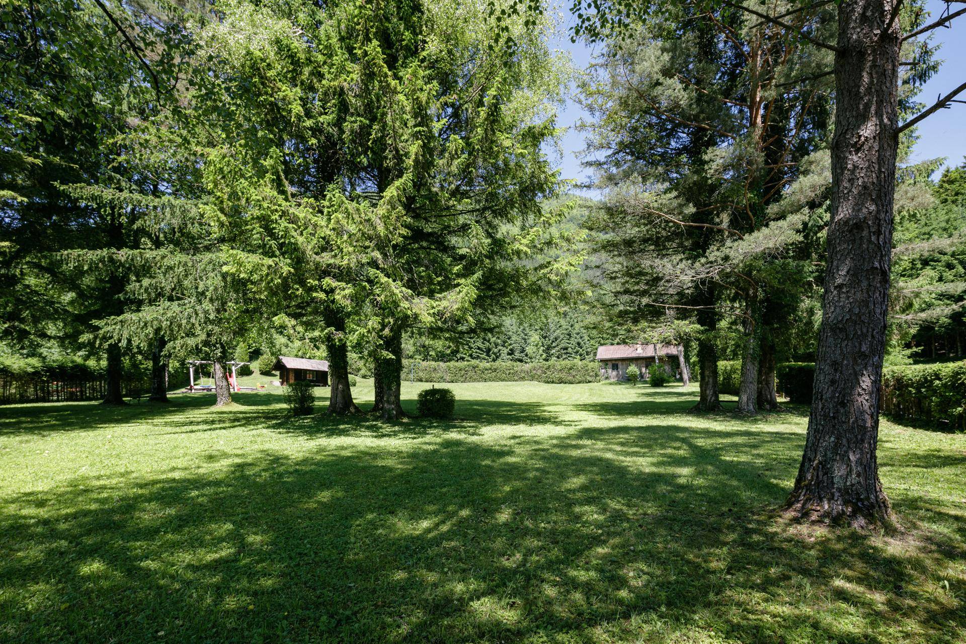 Weitläufiger Garten mit großer Rasenfläche, alten Bäumen und kleinen Holzhäusern im Hintergrund.