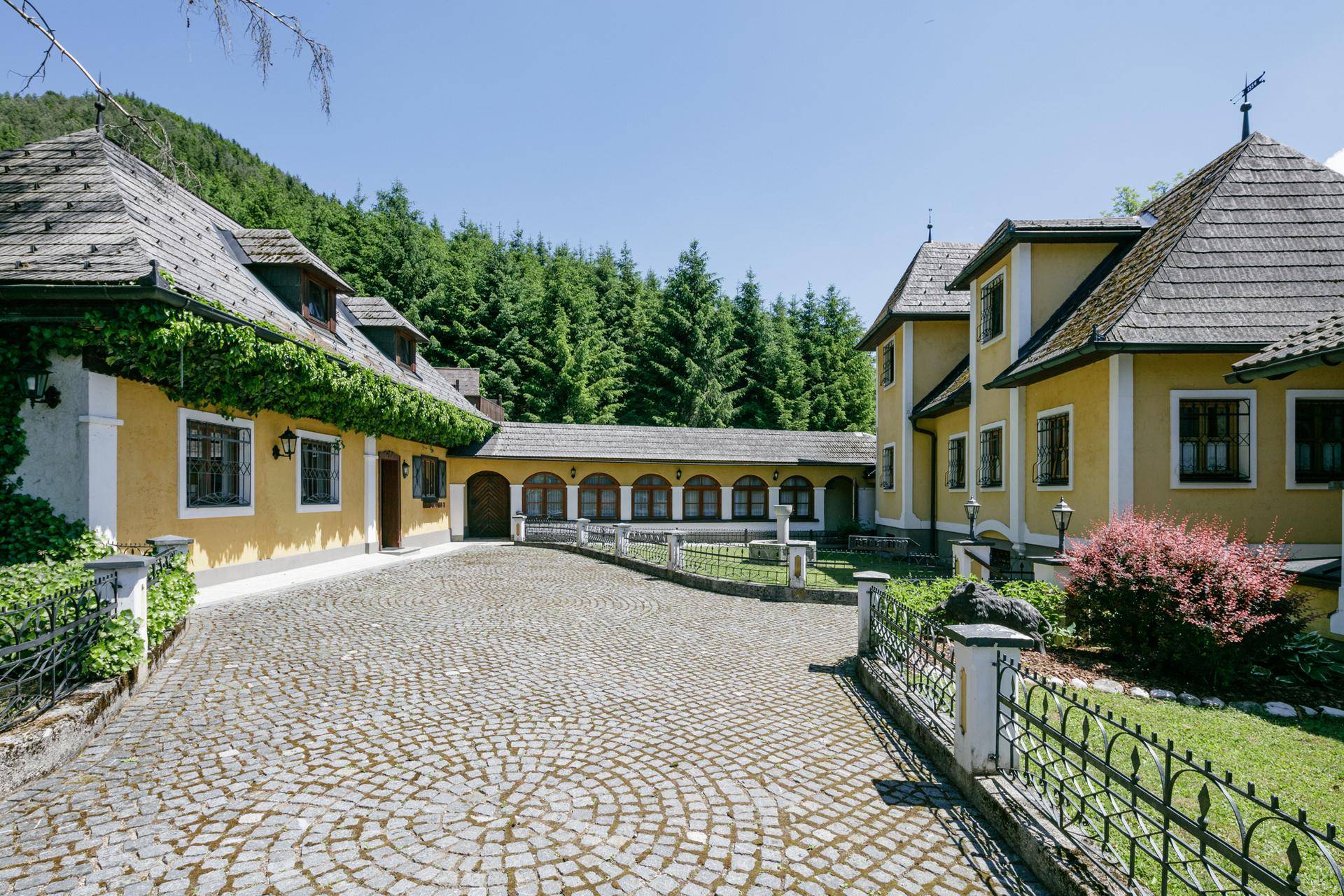 Historischer Gebäudekomplex mit Kopfsteinpflaster-Hof und umgebender Natur.