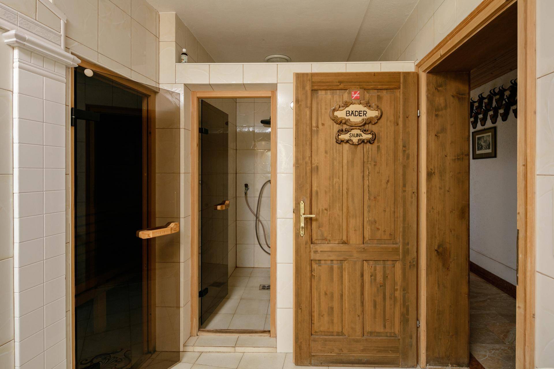 Eingangsbereich zum Wellnessbereich mit Holztür, Sauna und Duschkabine, alles gefliest.