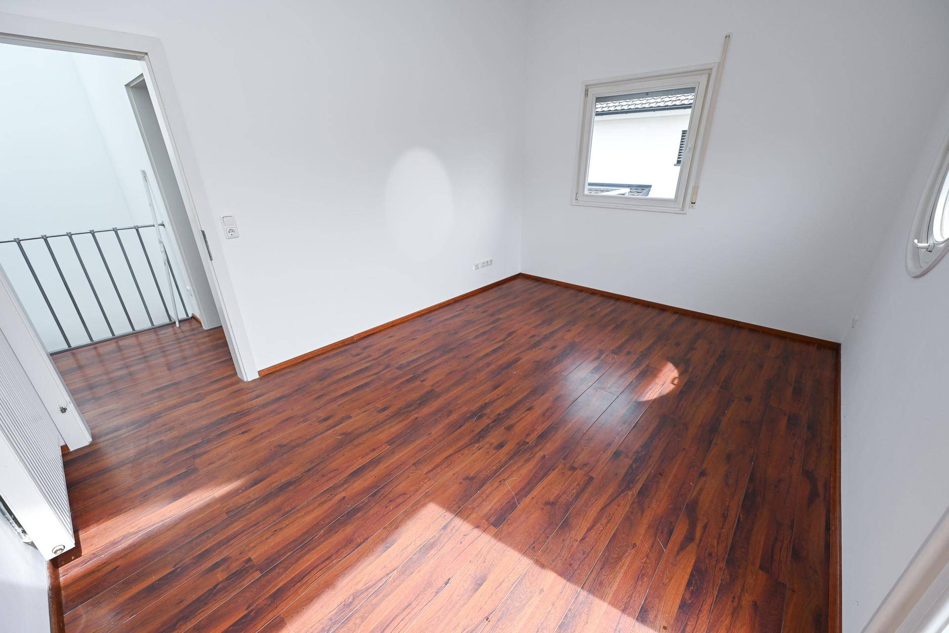 Helles Zimmer mit Laminatboden und Fenster mit Blick nach draußen.