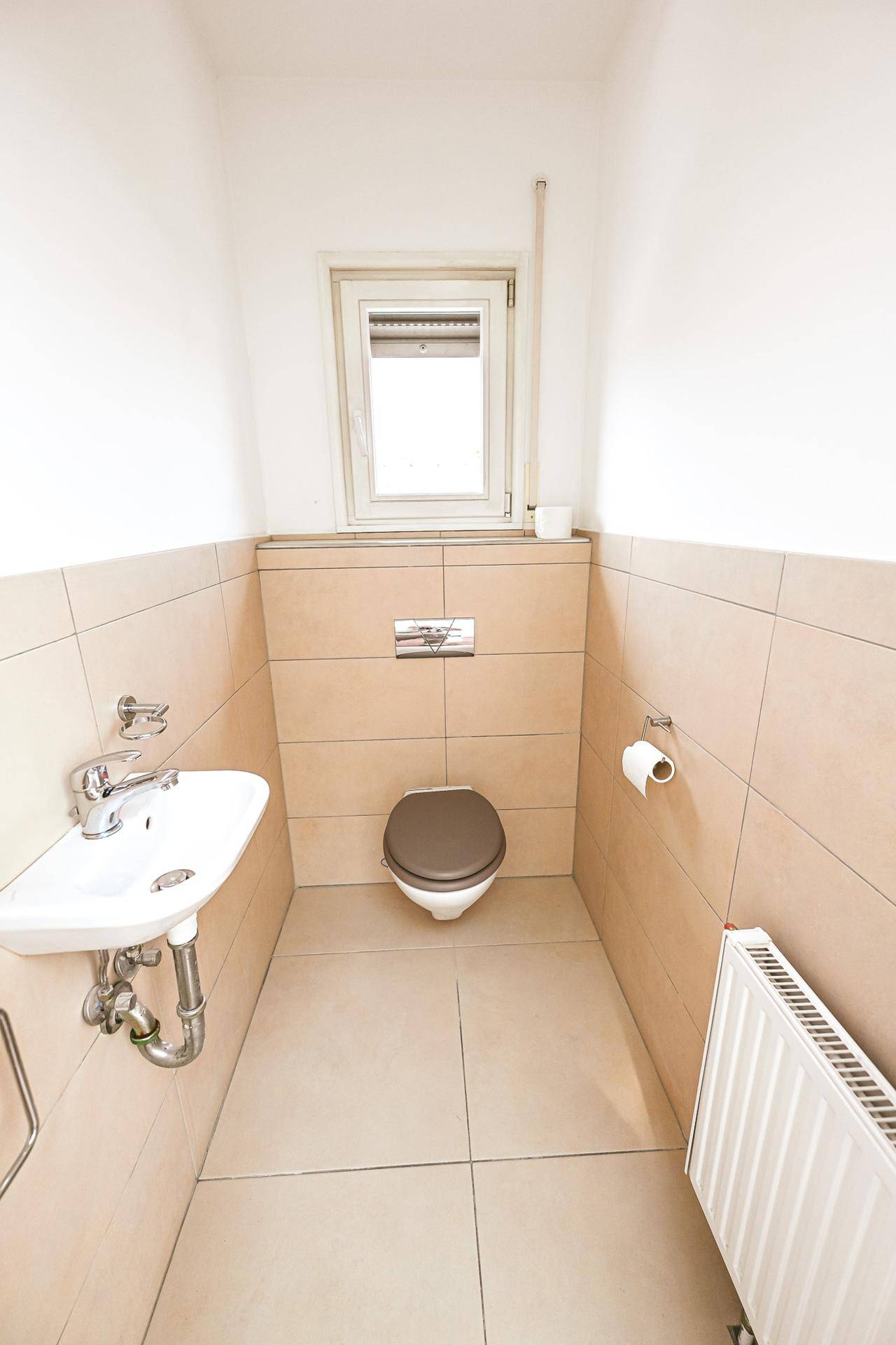 Separate Gästetoilette mit Fenster, Waschbecken und Heizkörper.