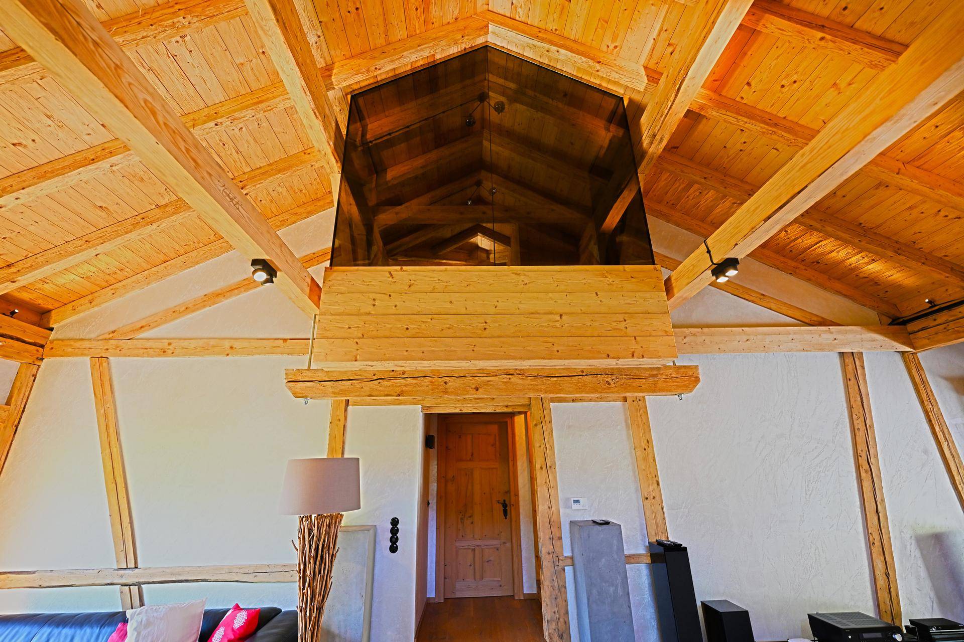 Beeindruckende Holzbalkendecke mit verglaster Galerie und rustikaler Holztür, die den Raum öffnet.