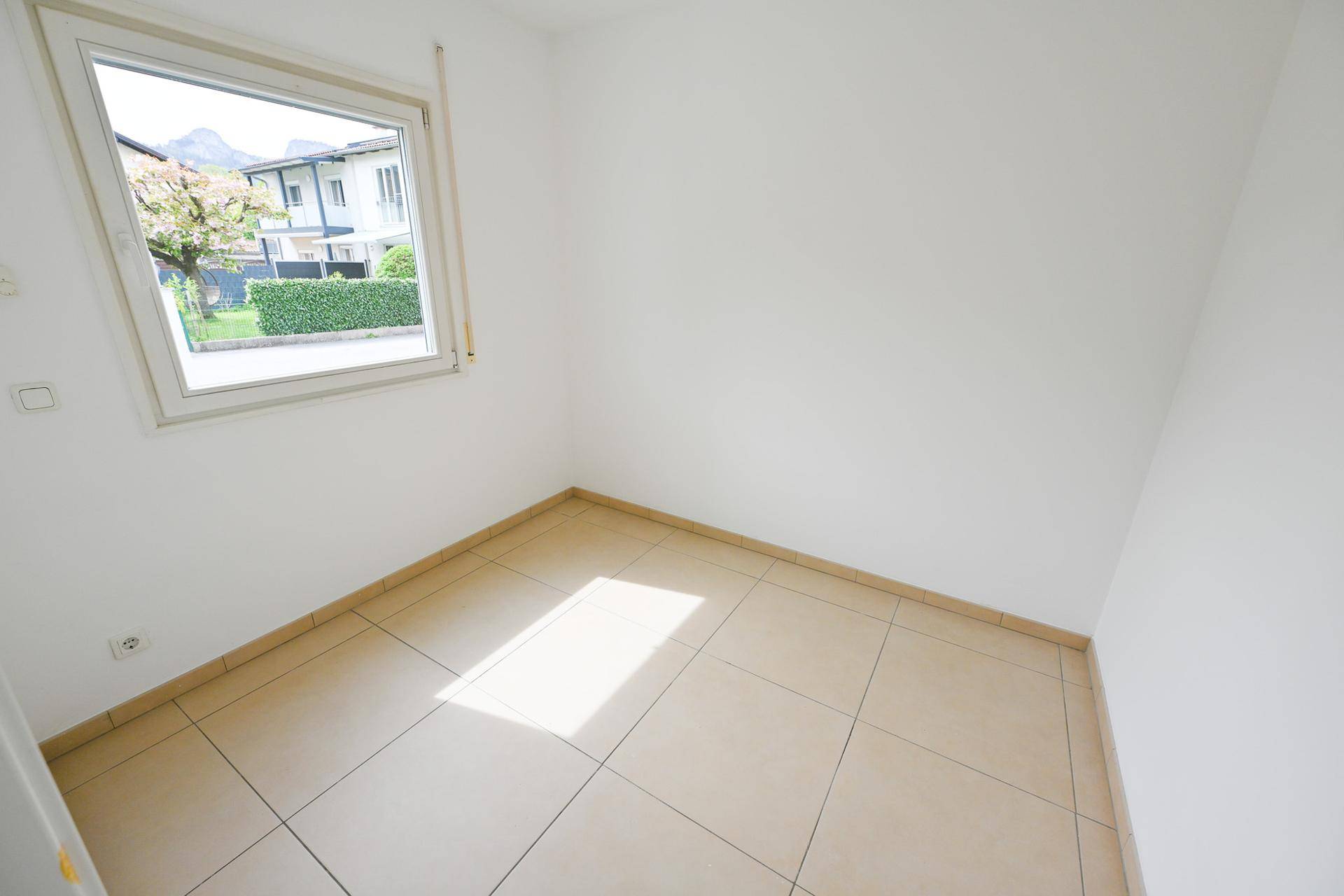 Helles Zimmer mit Fliesenboden und Fenster mit Blick ins Grüne.