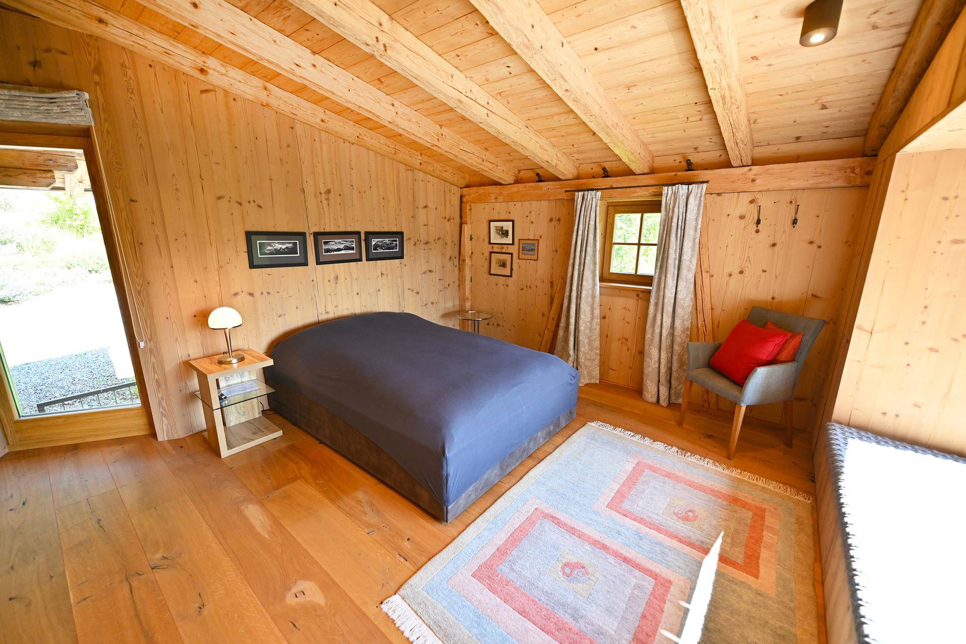 Helles Schlafzimmer mit Holzwänden, Holzbalkendecke und Zugang zum Außenbereich.