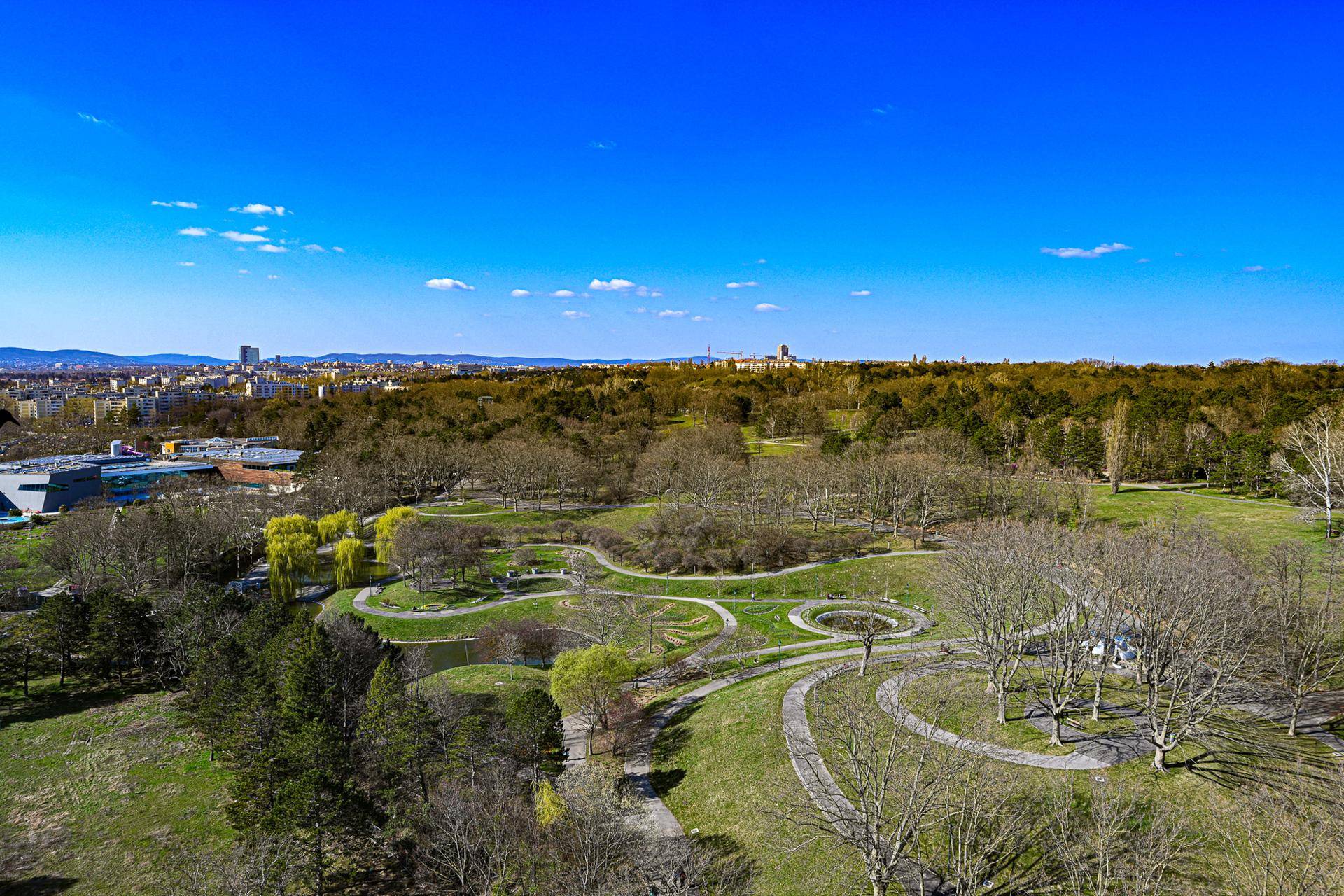 Weitläufiger Park mit Grünflächen und Wegen, umgeben von städtischer Bebauung.