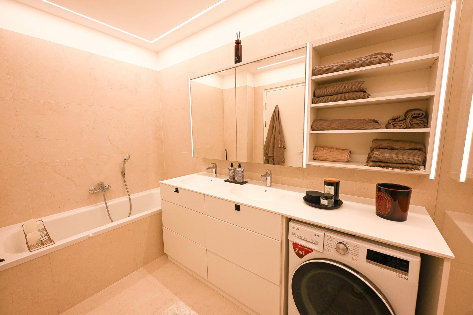 Geräumiges Badezimmer mit Badewanne, Doppelwaschbecken und integrierter Waschmaschine.