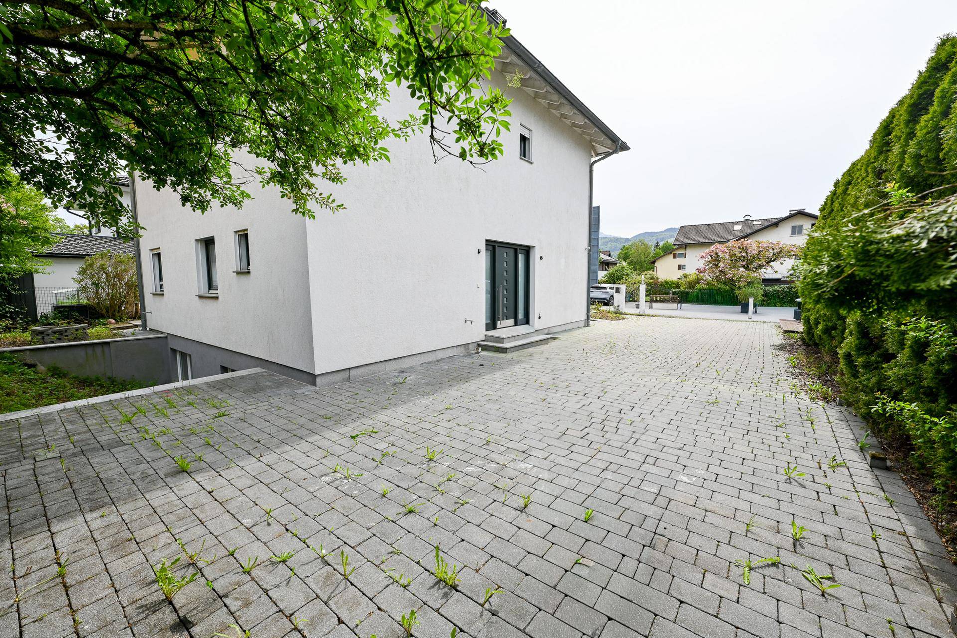 Seitenansicht des Hauses mit breiter Auffahrt und Zugang zum Untergeschoss.